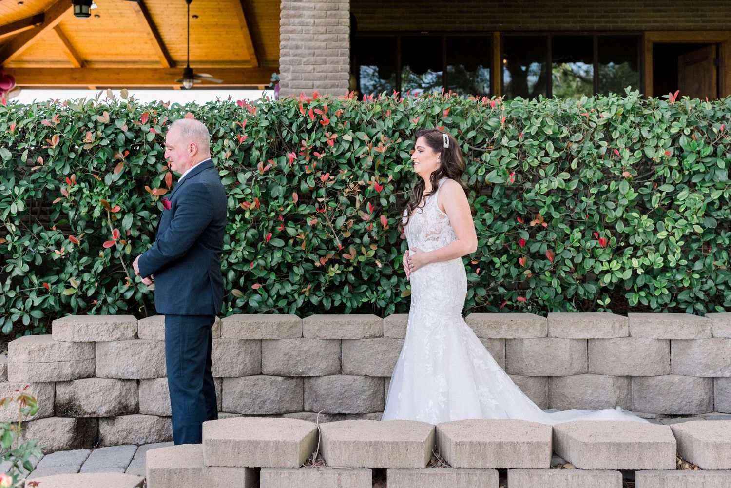 A wedding first look moment between a couple standing on stone steps with a lush green hedge background.