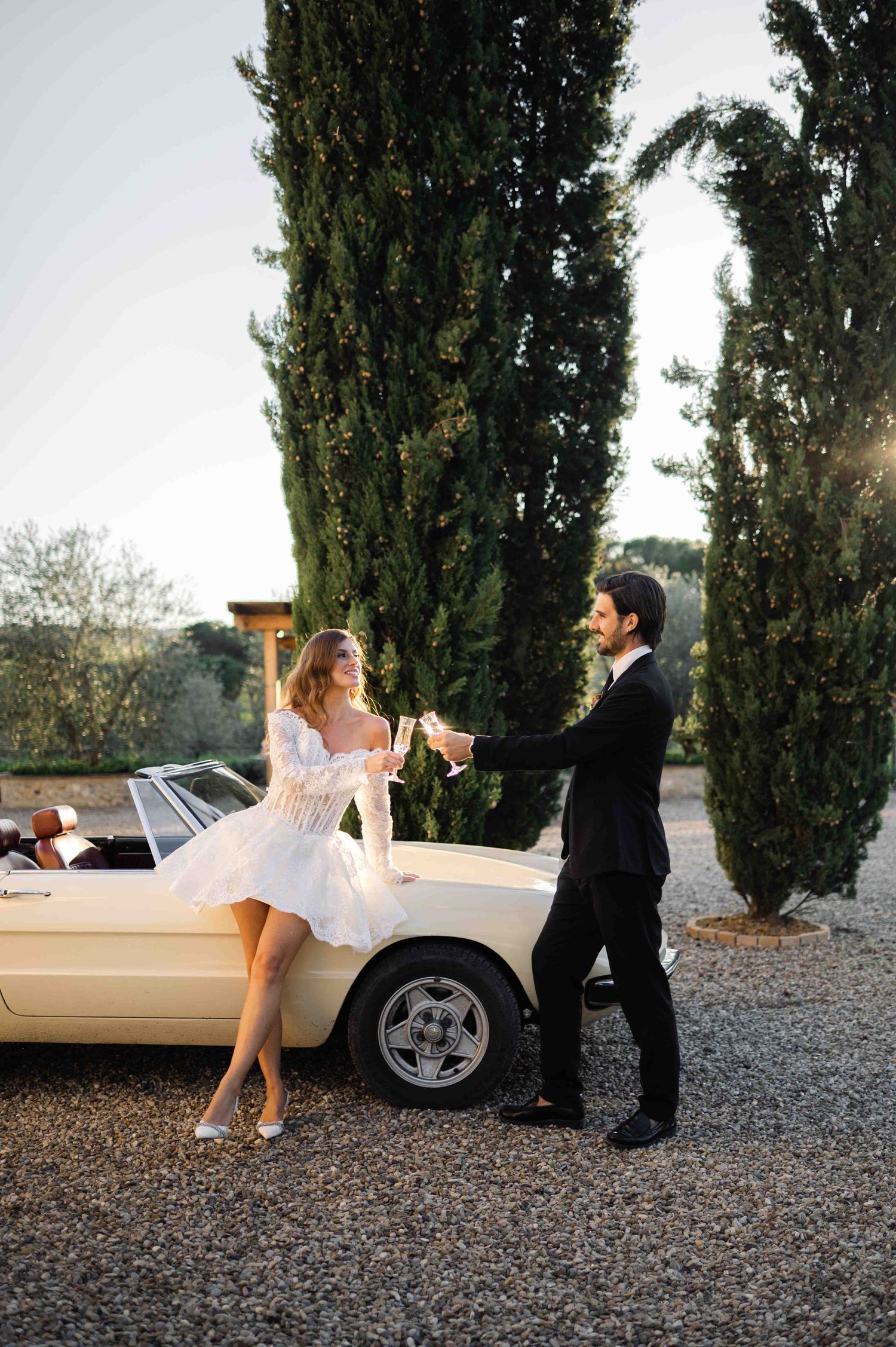 Wedding couple posing playfully near vintage car.