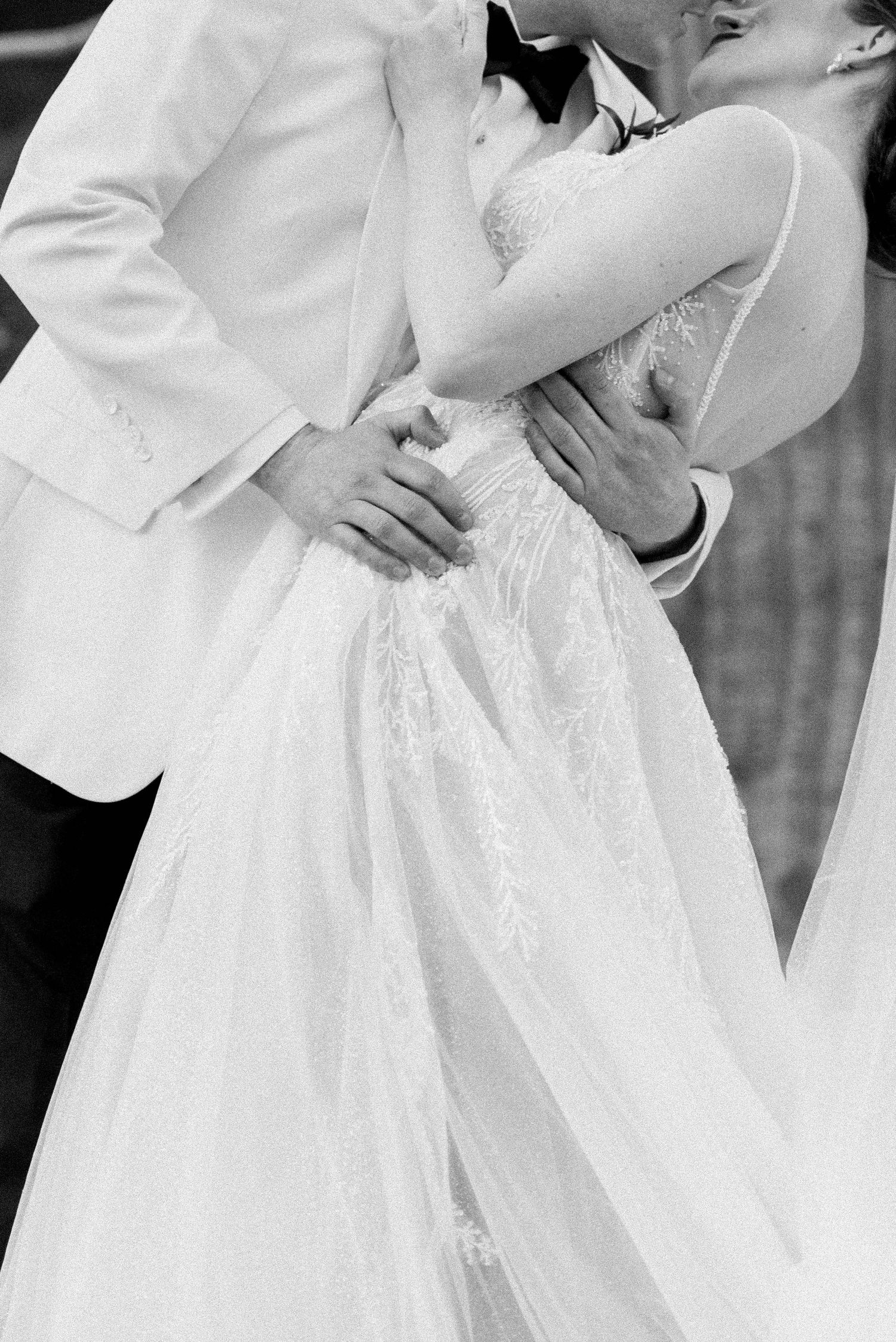 Close up black and white detail shot of couple embracing in formal wedding attire.