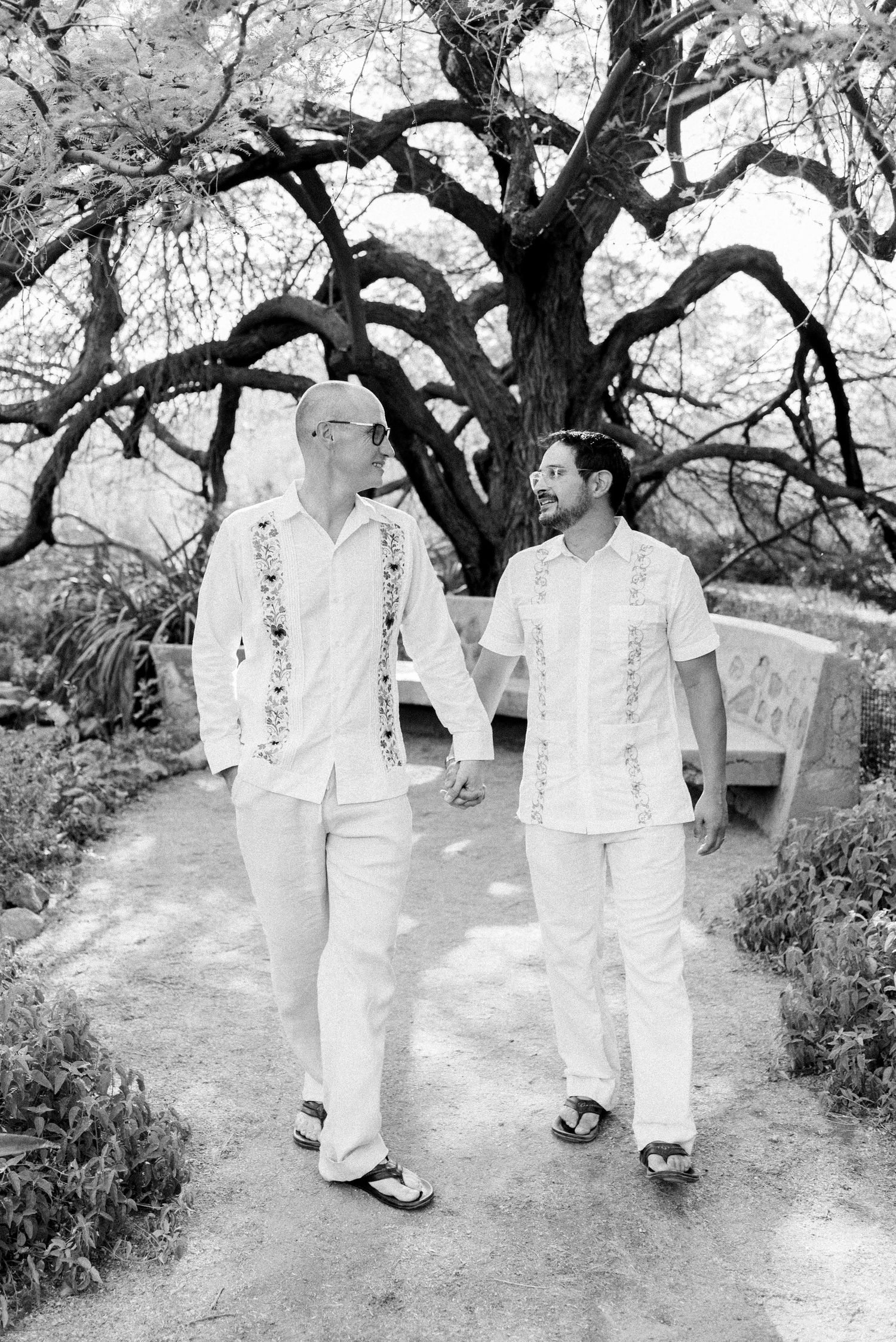 Four black and white photographs show two people in white clothing walking together on a garden path under trees.