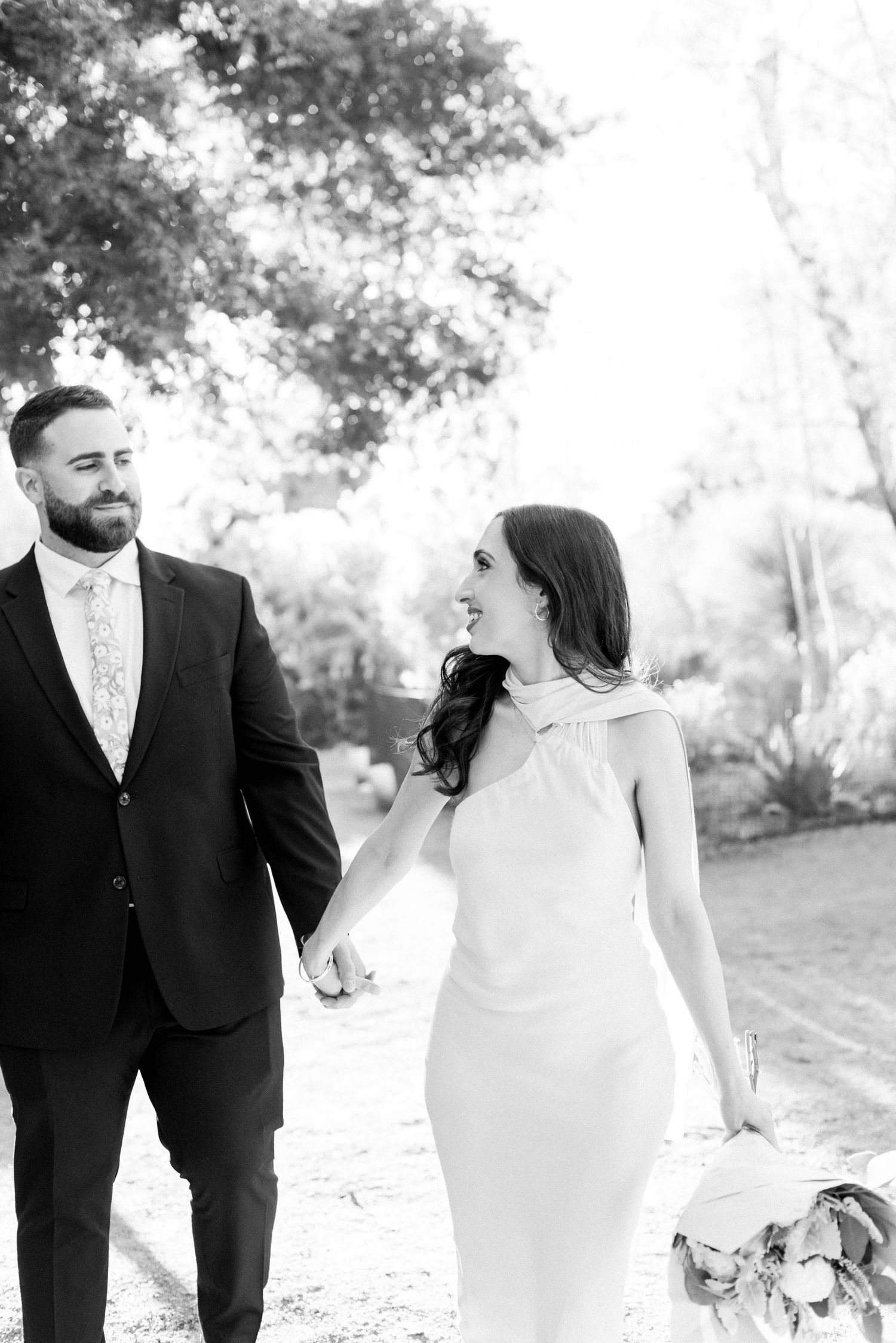 A romantic black and white wedding photo series showing a couple in formal attire walking together outdoors.