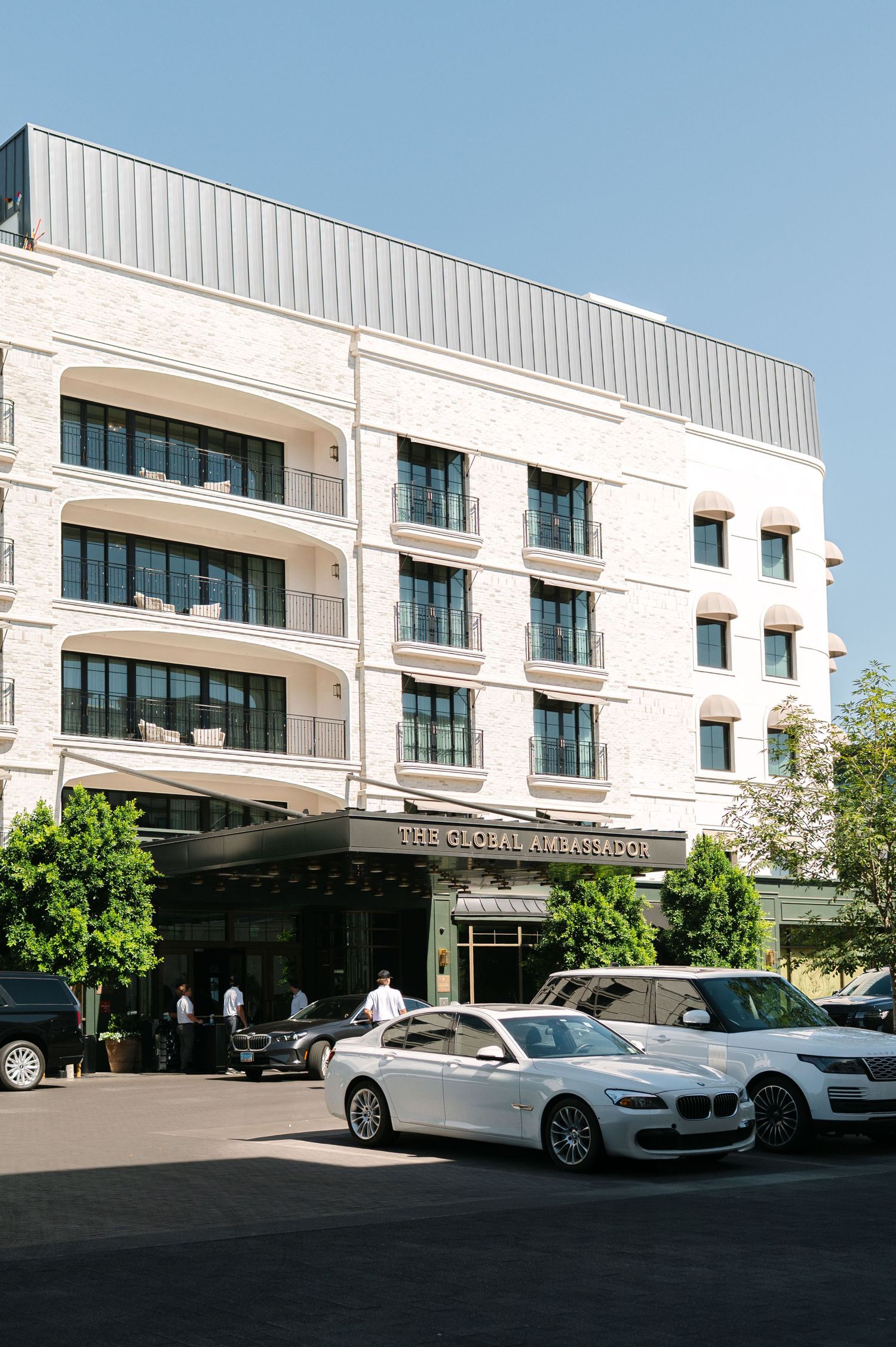 Modern white commercial building exterior with luxury vehicles parked under covered driveway entrance.
