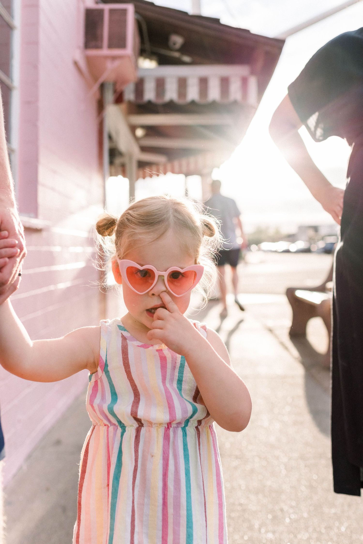 A toddler in a striped sundress plays outdoors in warm sunlight, creating a series of connected photos.