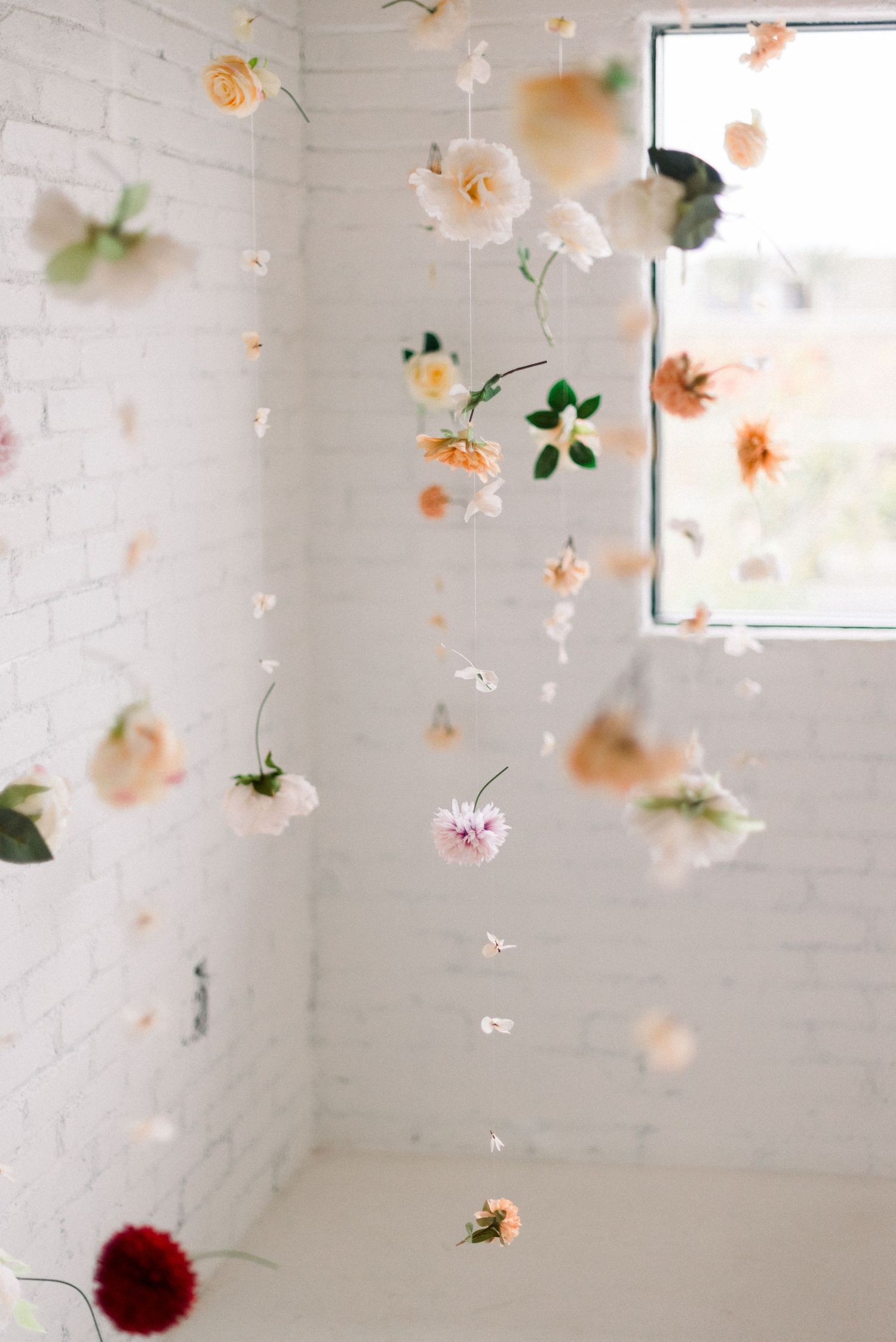 Hanging floral installation with roses and scattered petals against white brick wall and window.