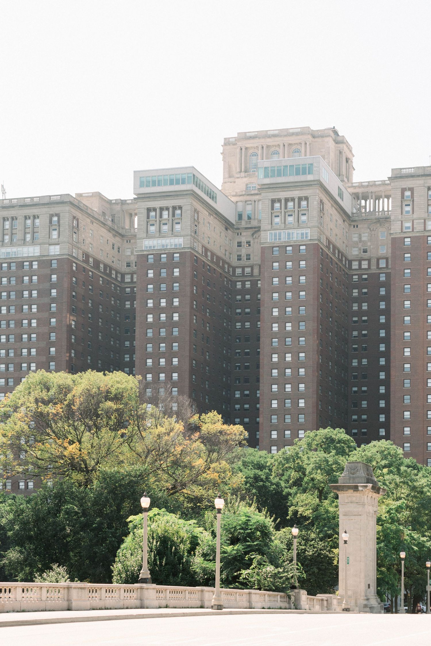 Tall historic brick hotel building rises above green trees in an urban setting.