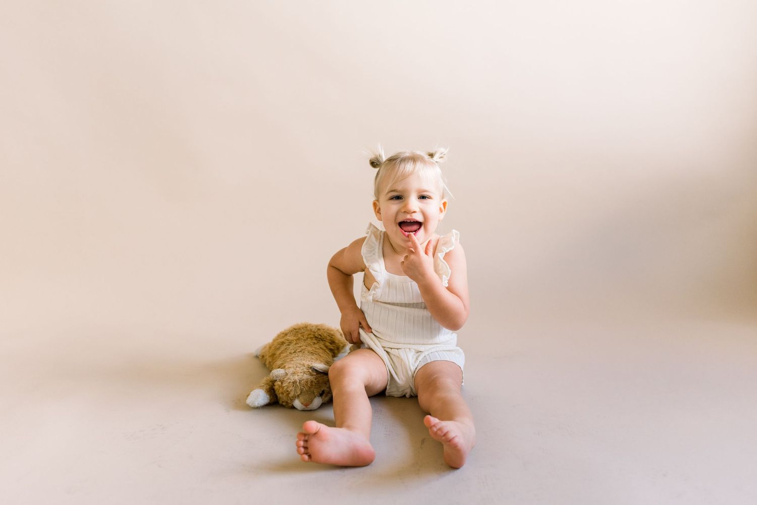 A happy toddler sitting with a plush teddy bear on beige background.
