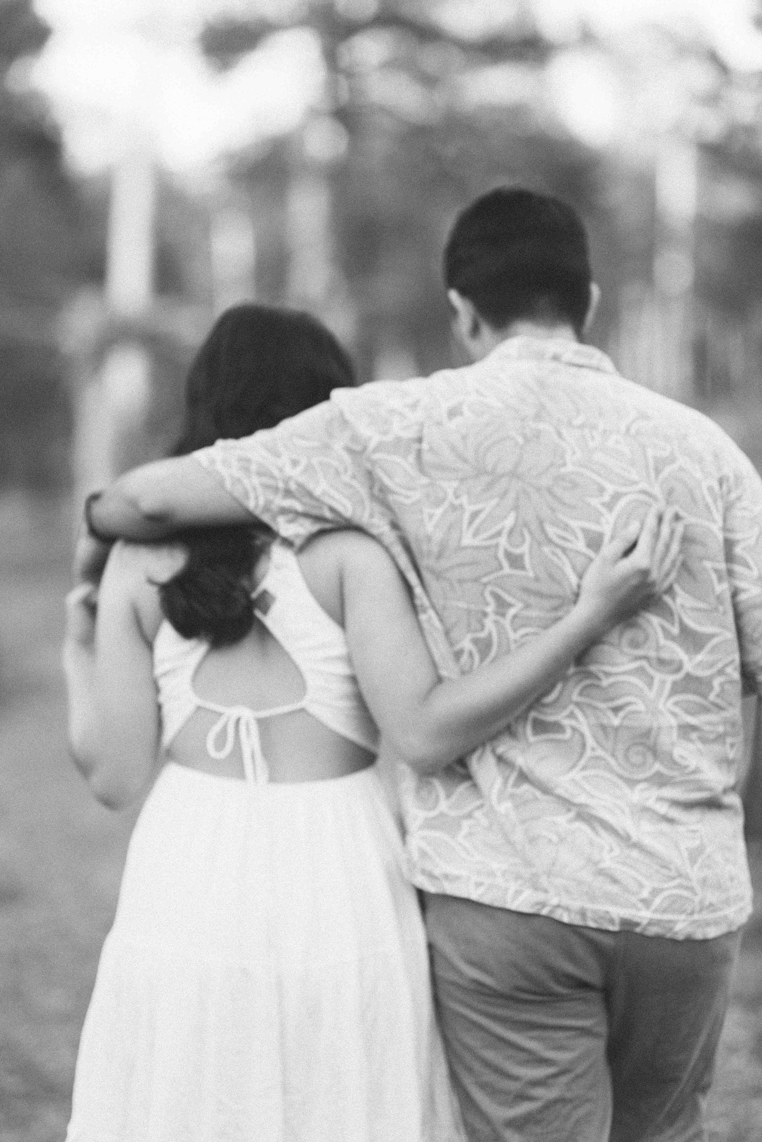 A black and white photo captures a couple walking away together through a forest setting.
