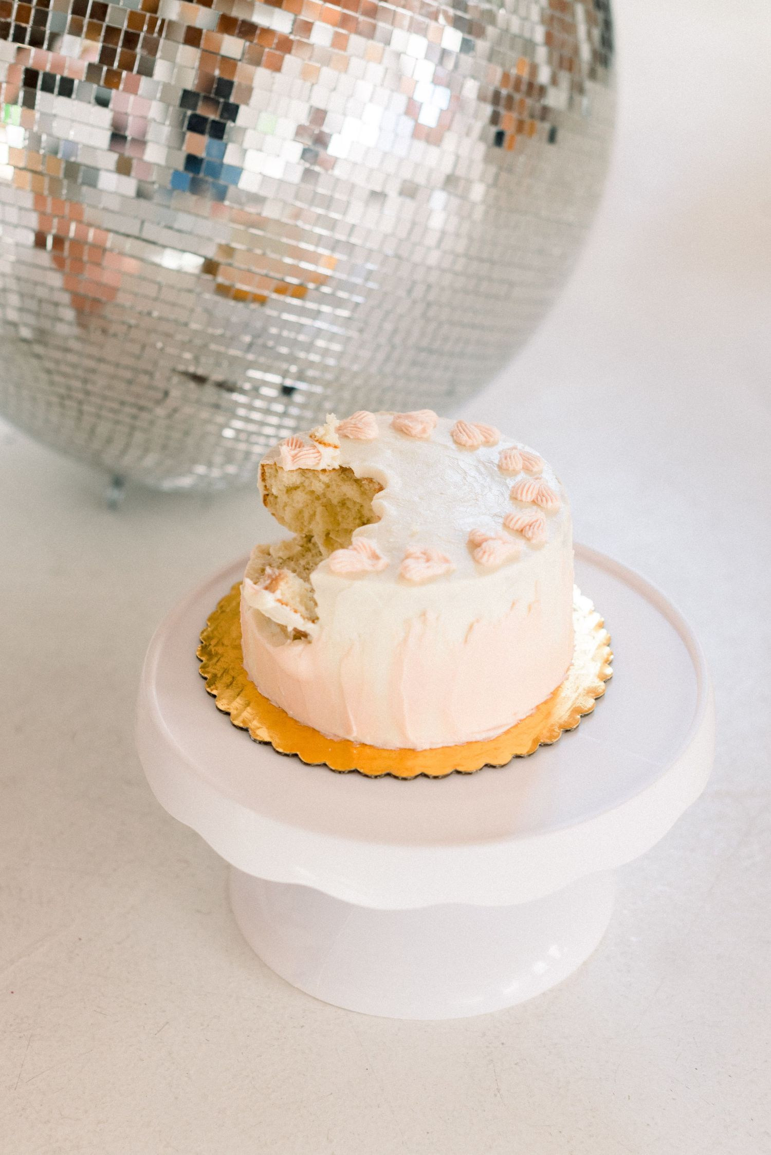 White frosted cake with bite taken out displayed next to silver disco ball.