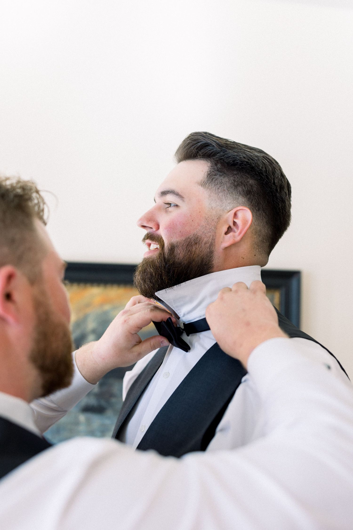Groomsman adjusts bowtie while helping with wedding preparation in formal attire.