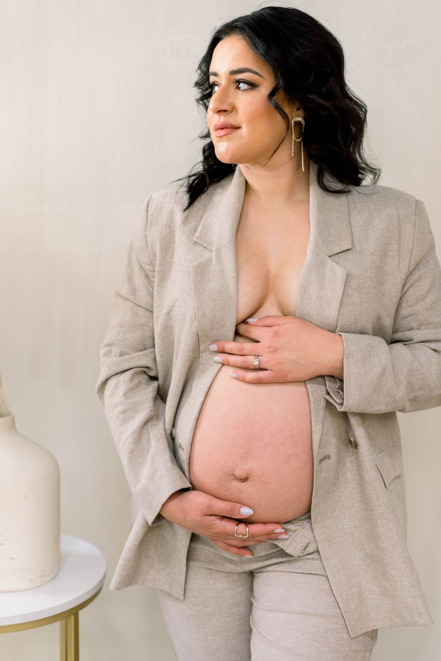 Maternity photo of woman in beige blazer cradling baby bump.