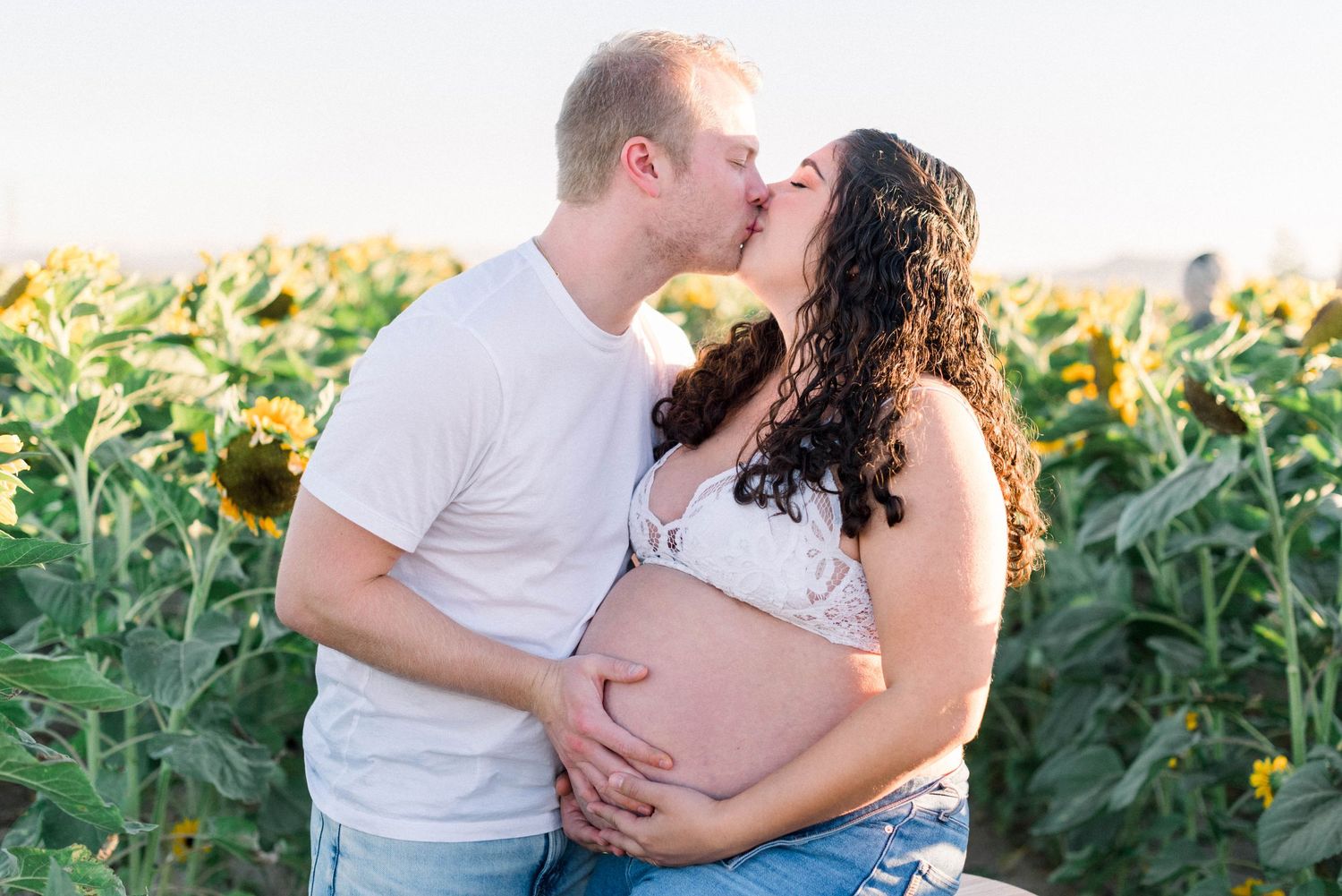 Maternity photo of couple kissing in sunflower field
