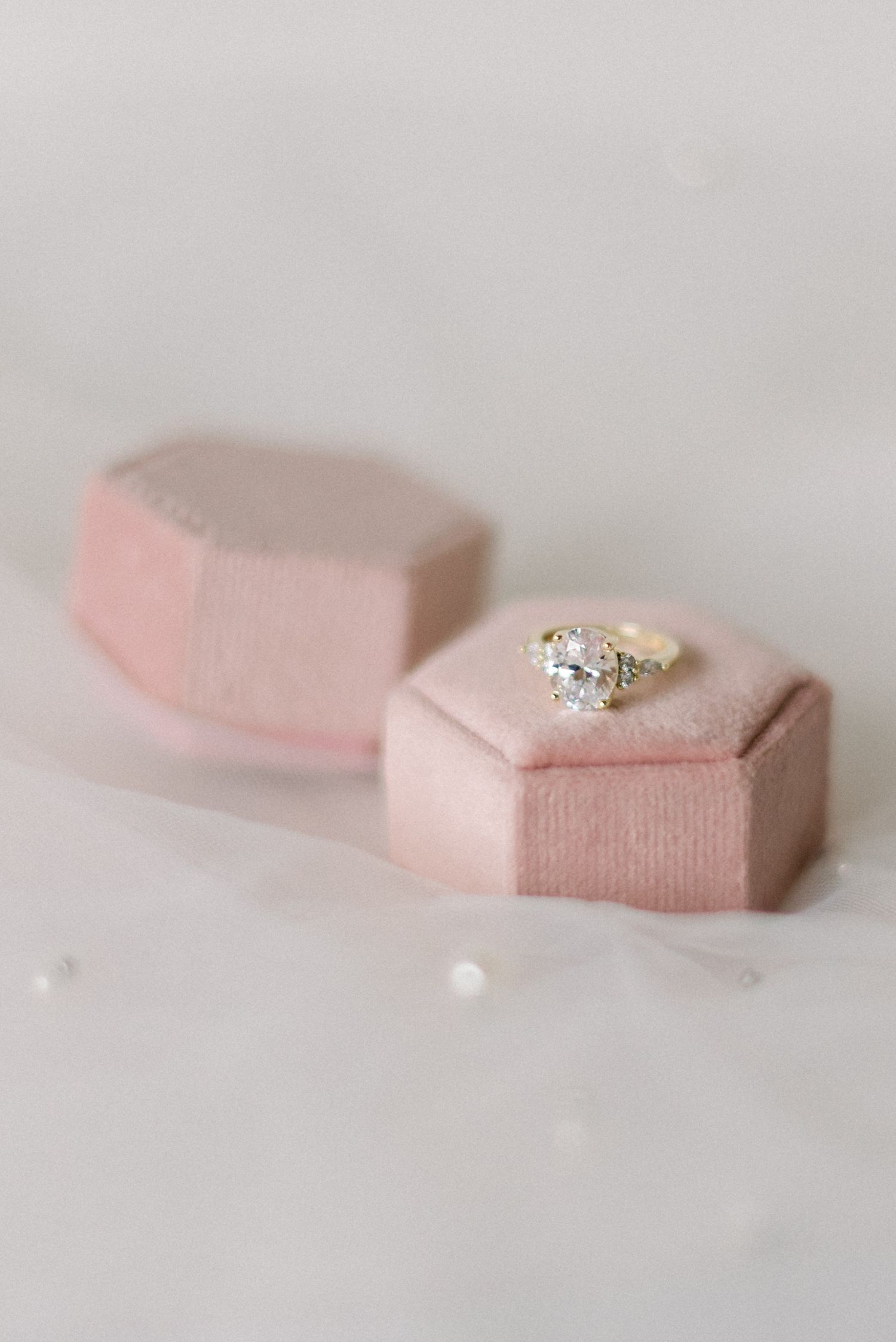 Two pink velvet ring boxes with a sparkling diamond ring on display.