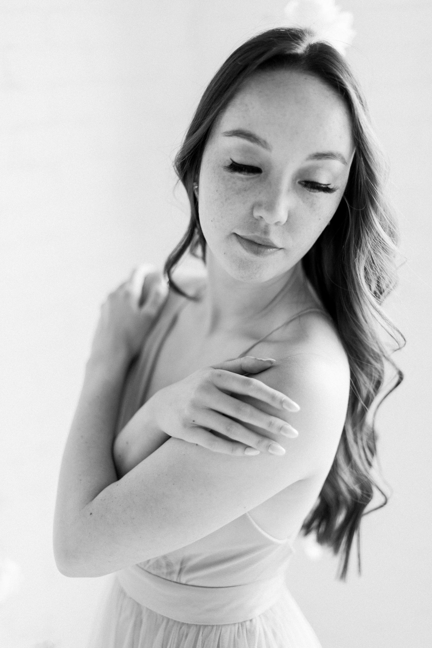 Intimate black and white portrait showing gentle self-embrace in soft lighting.