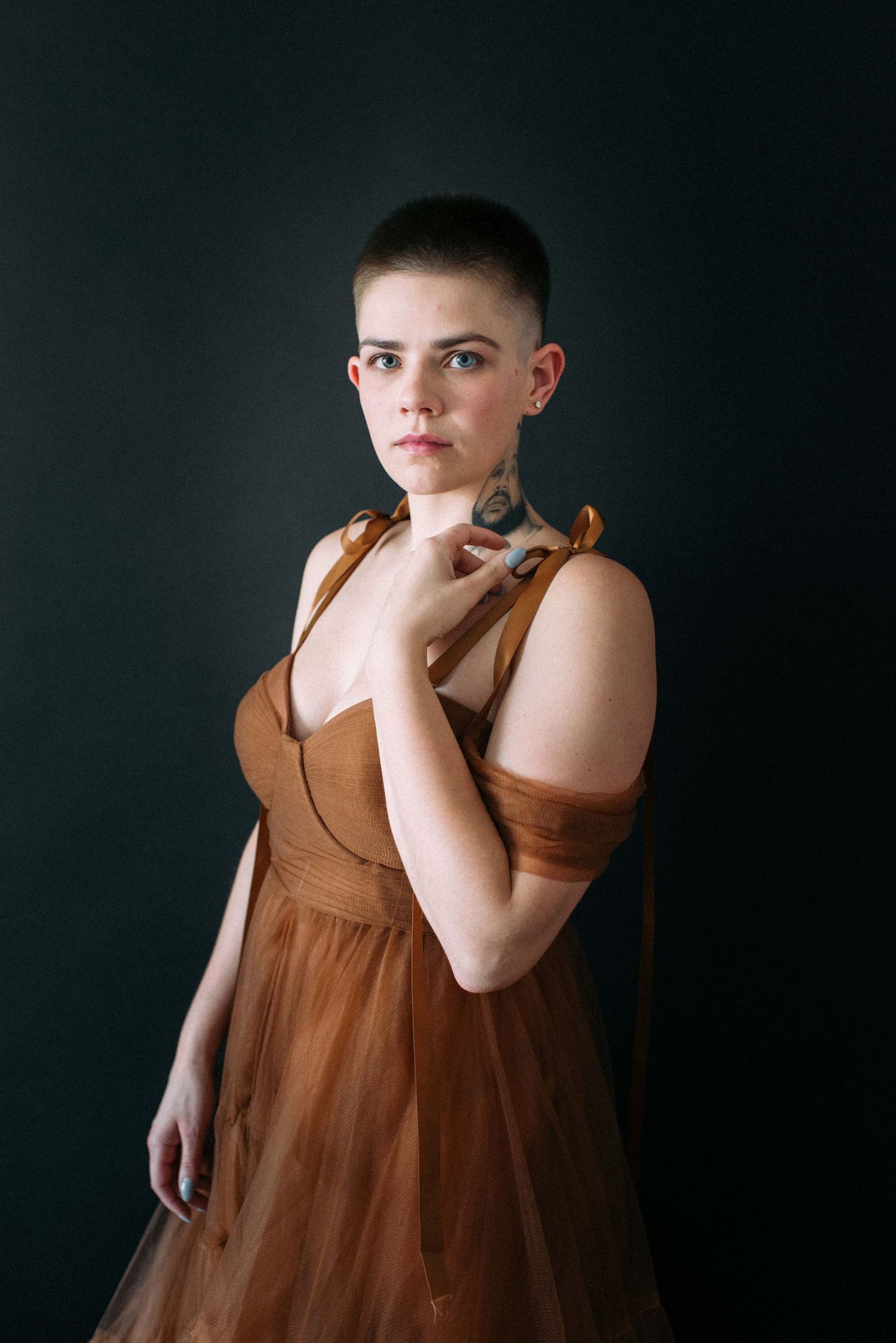 A studio portrait featuring someone in an elegant brown dress against a dark backdrop.