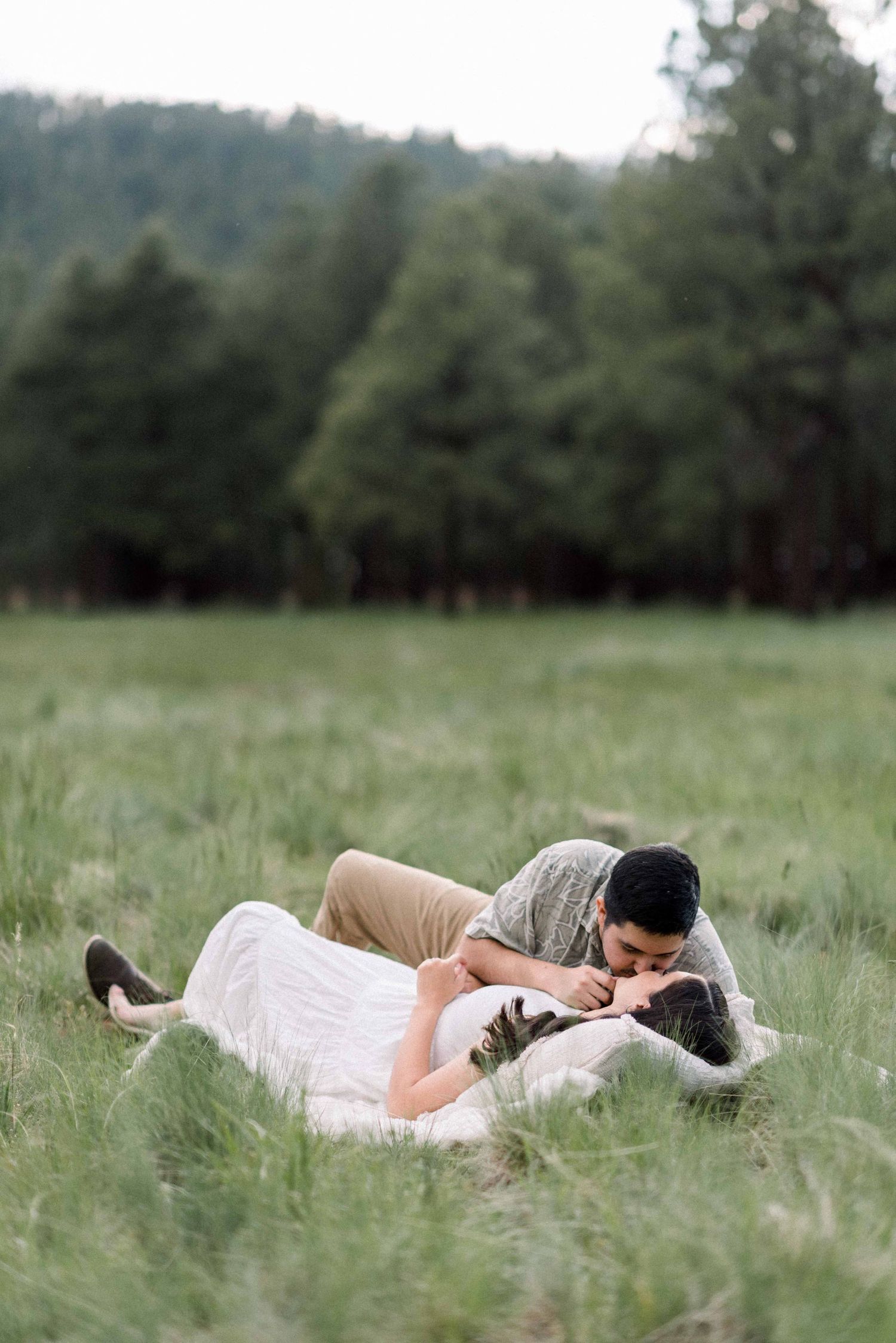 Intimate couple portrait on blanket in sunlit meadow surrounded by forest.