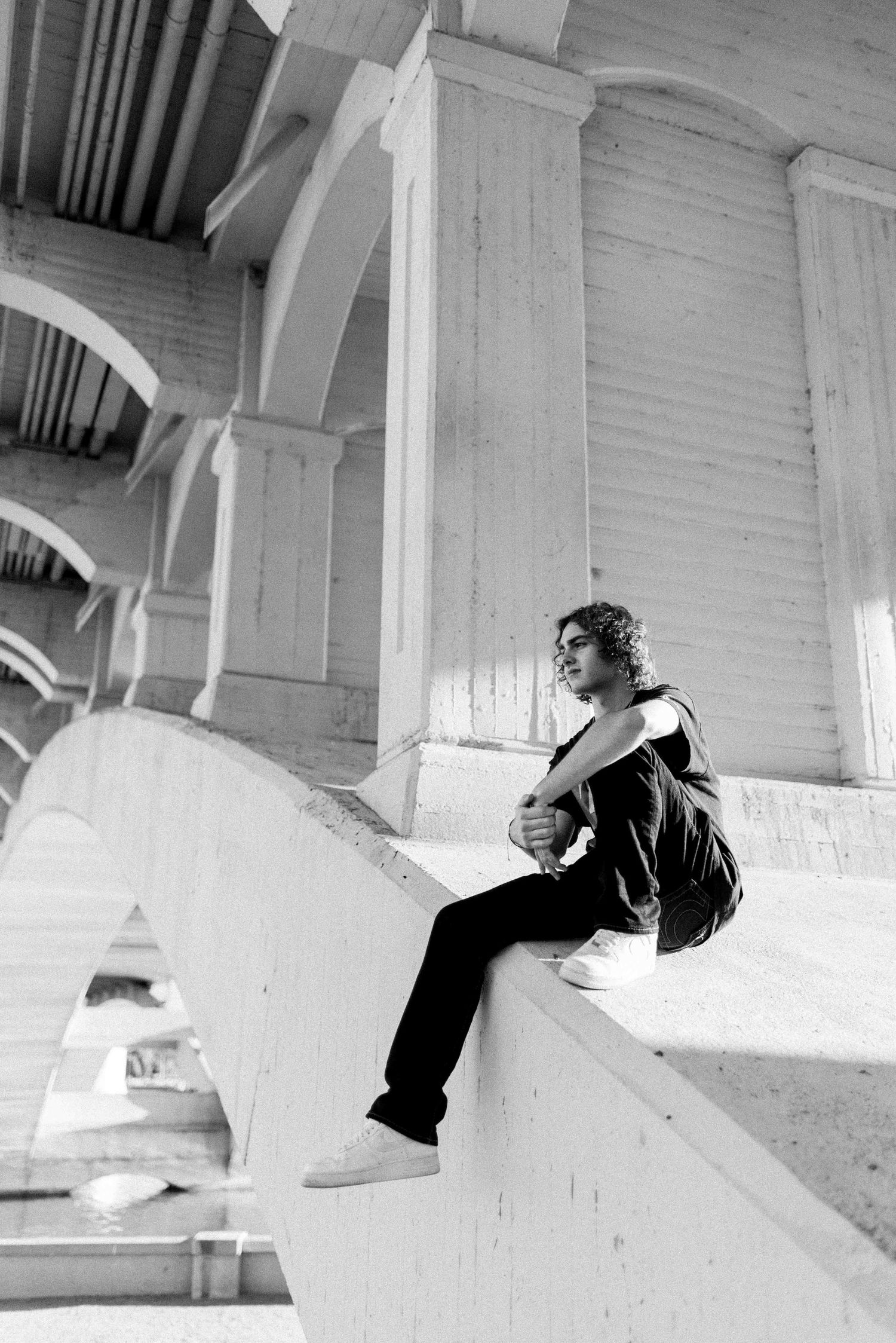 Black and white photo of person sitting on architectural steps with arches in background.