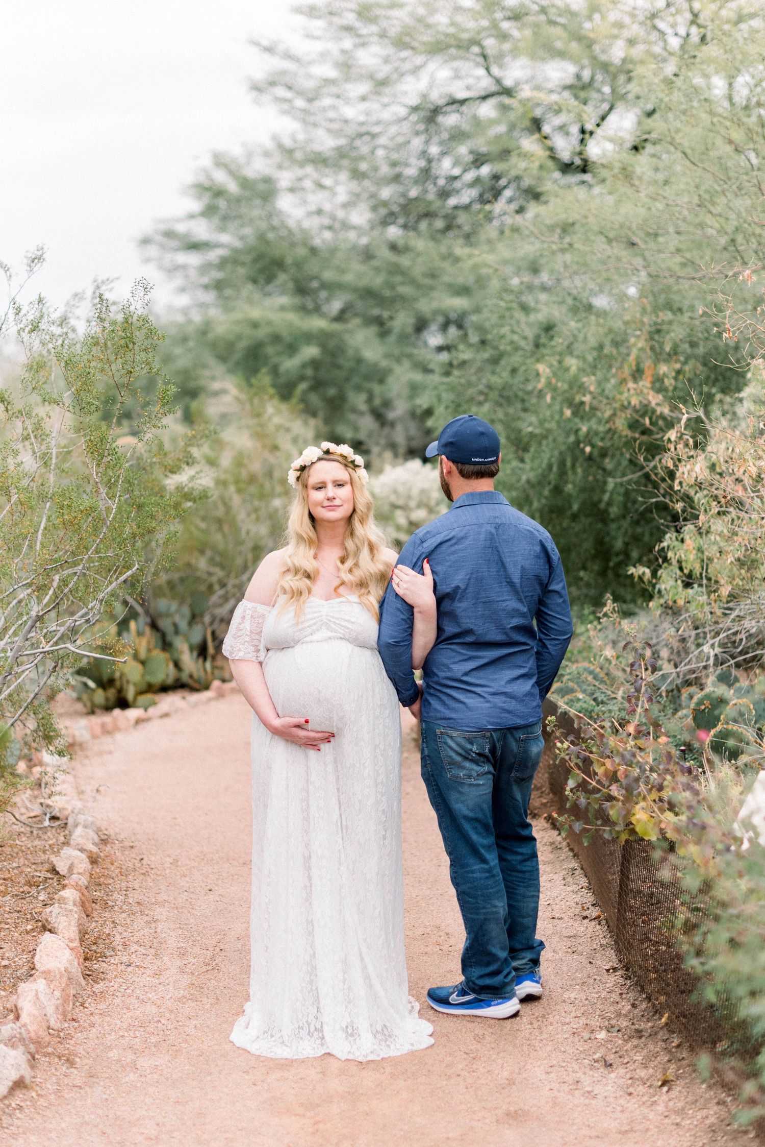 Maternity photoshoot in a desert garden path featuring a white lace dress and floral crown.