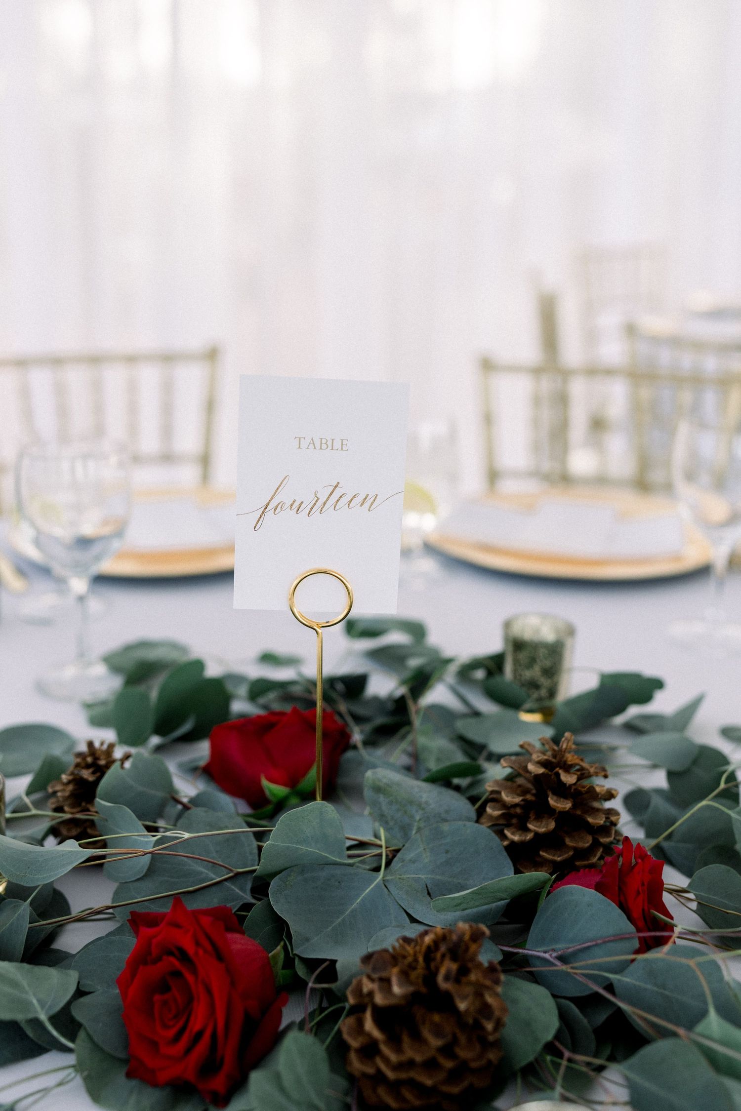 Winter wedding centerpiece with red roses, pinecones and eucalyptus leaves around table number.