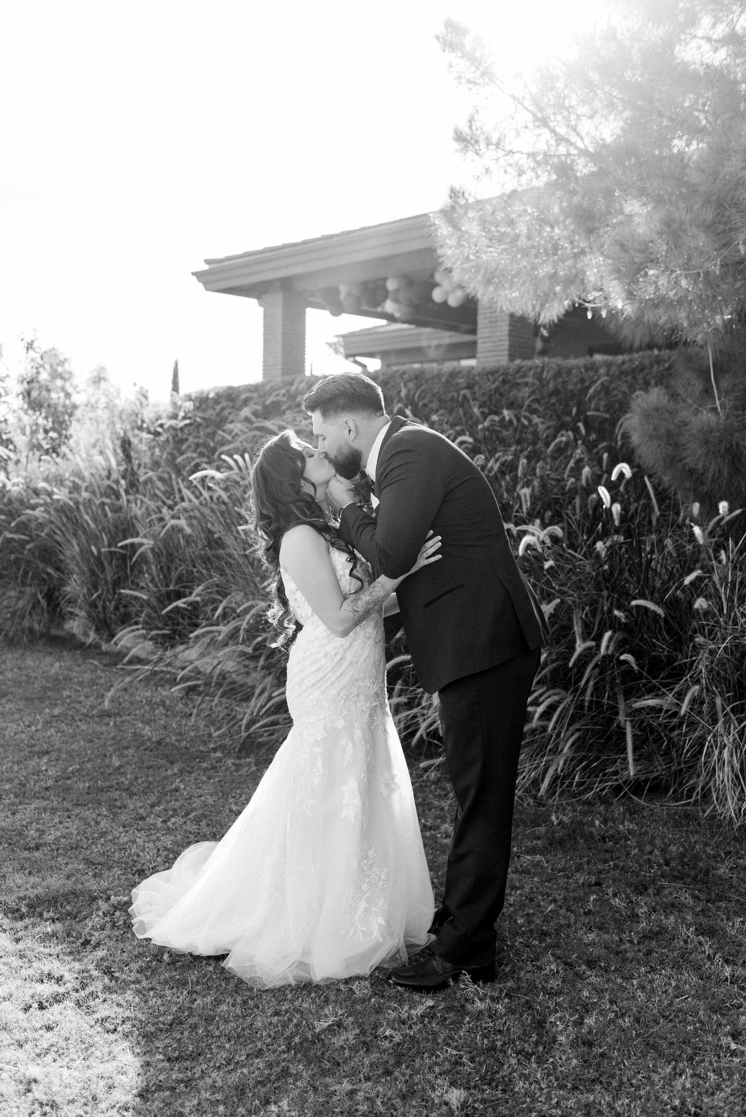 A romantic black and white wedding photo of a couple sharing their first kiss in a garden setting.