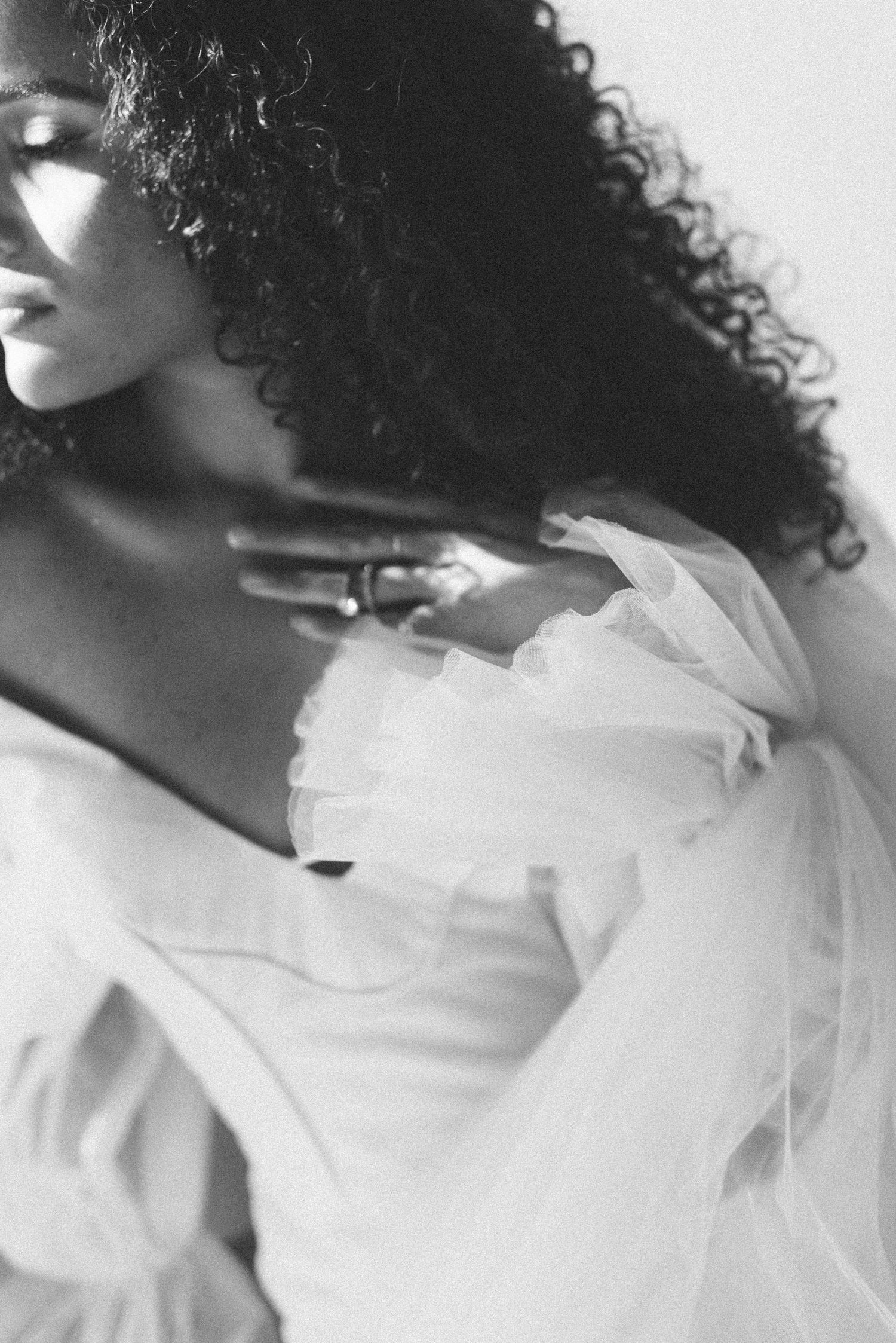 Dramatic black and white close-up of curly hair and white wedding dress details.