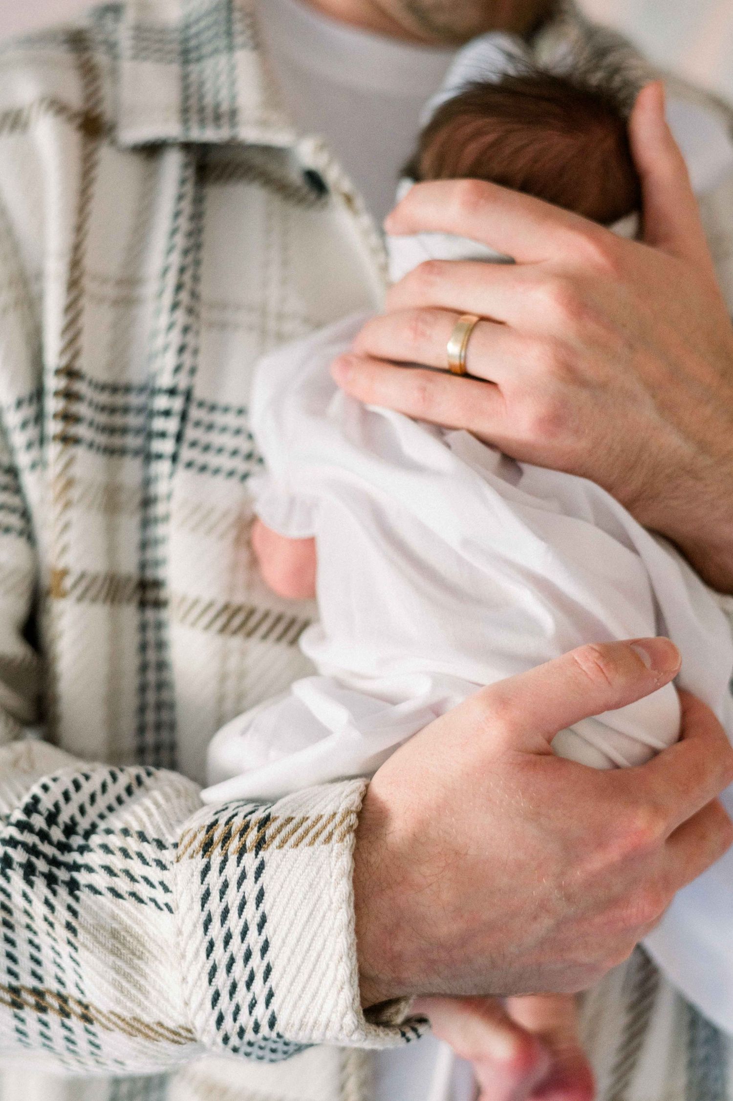 Close-up of parent in plaid shirt tenderly holding newborn wrapped in white.