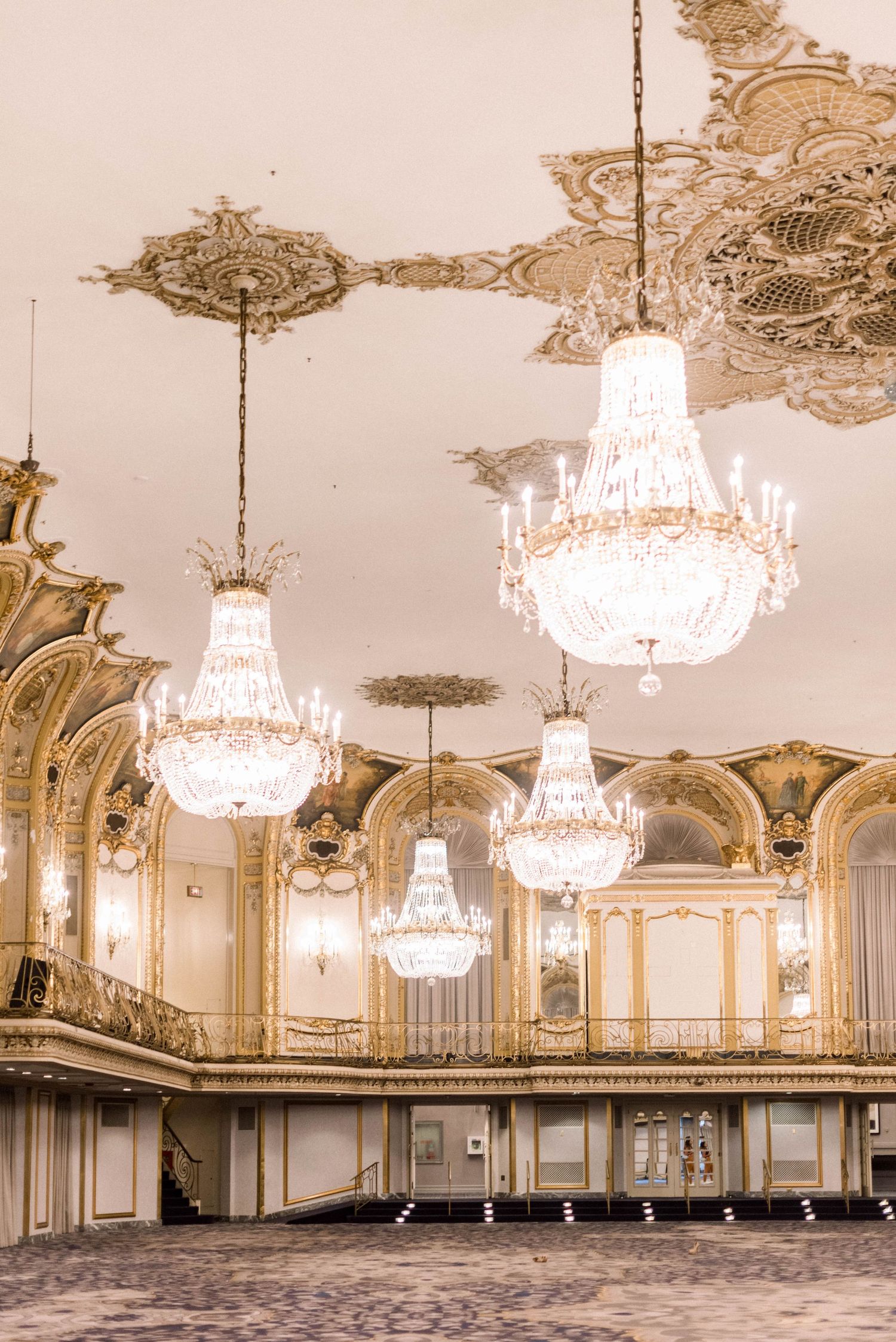 Opulent ballroom interior with multiple crystal chandeliers and ornate golden baroque details.