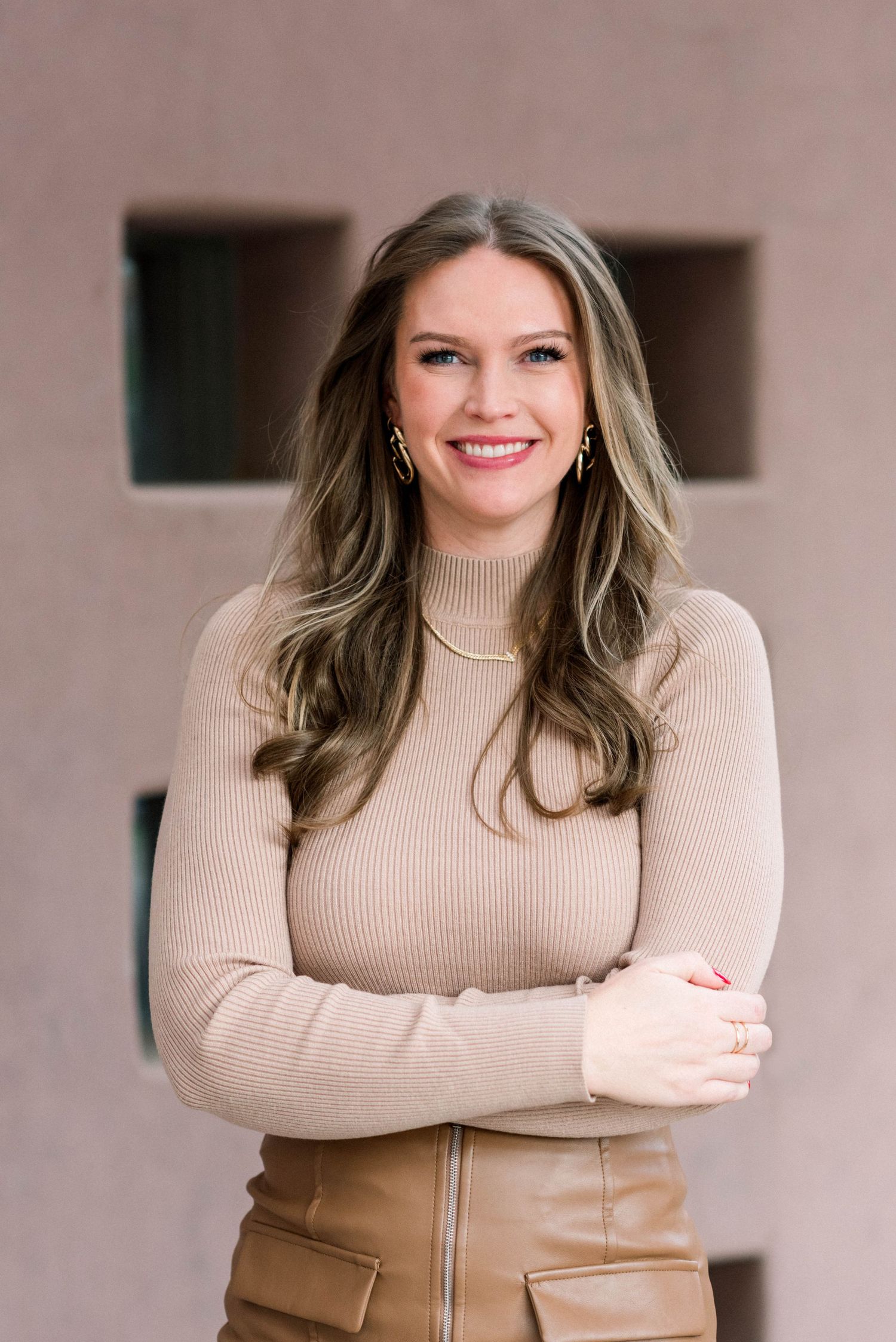 Modern fashion portrait showing beige sweater and tan leather skirt against textured wall.