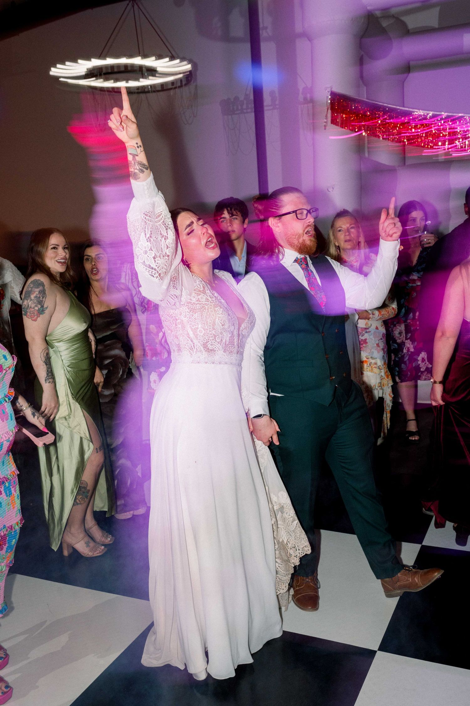 Wedding reception dance floor with guests celebrating under purple lighting.