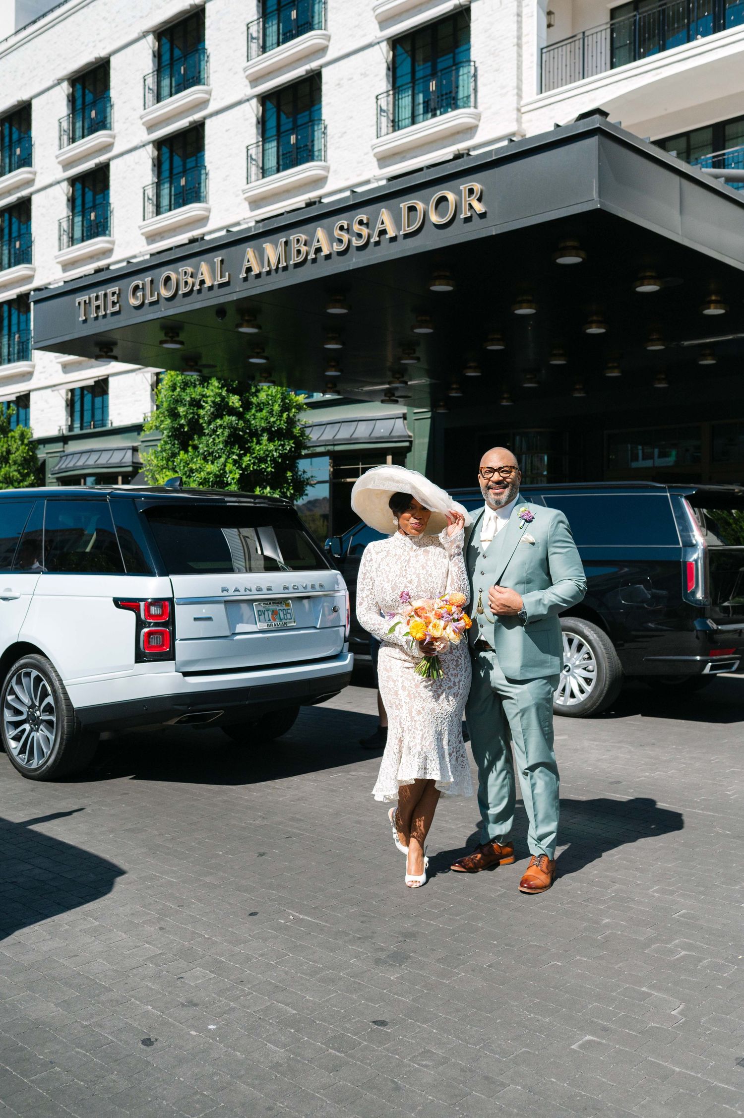 Wedding couple walking outside The Global Ambassador hotel entrance with luxury cars parked nearby.
