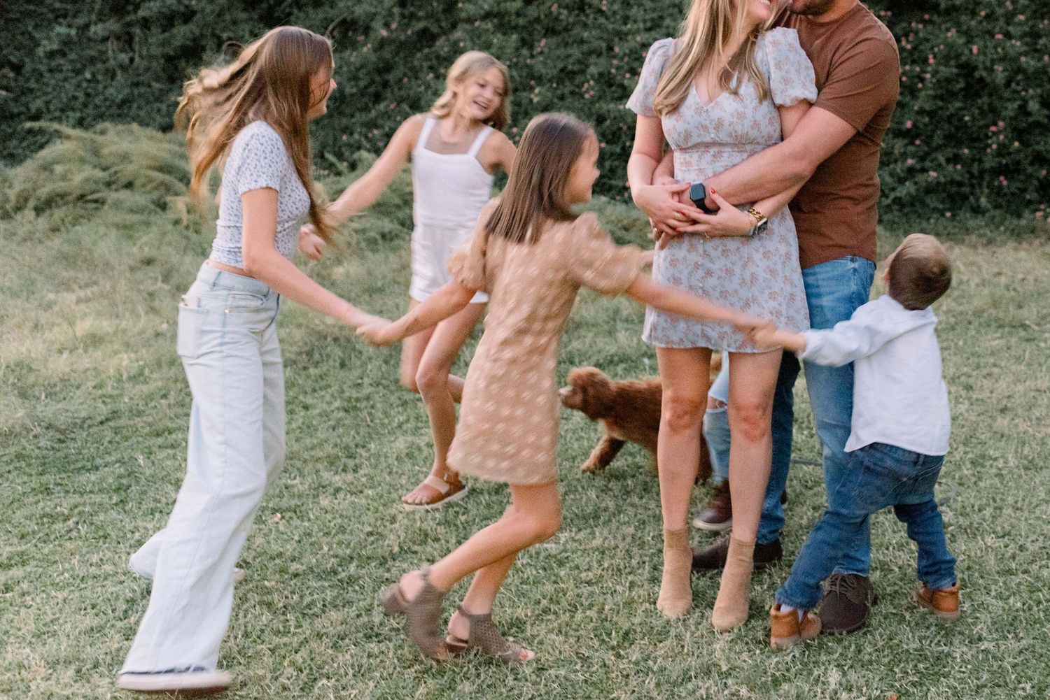 Family wearing coordinated brown and white outfits playing together in a grassy outdoor setting at sunset.