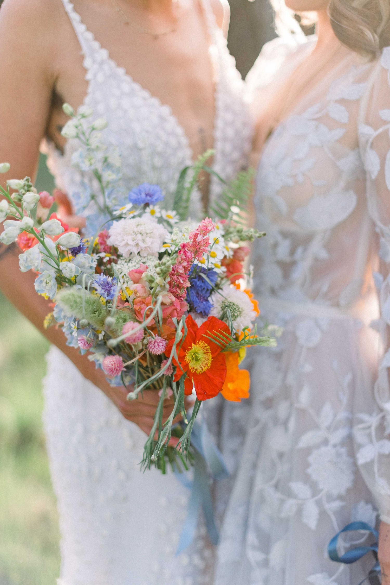 Detail shot of two wedding dresses and vibrant bouquets featuring orange poppies and wildflowers.