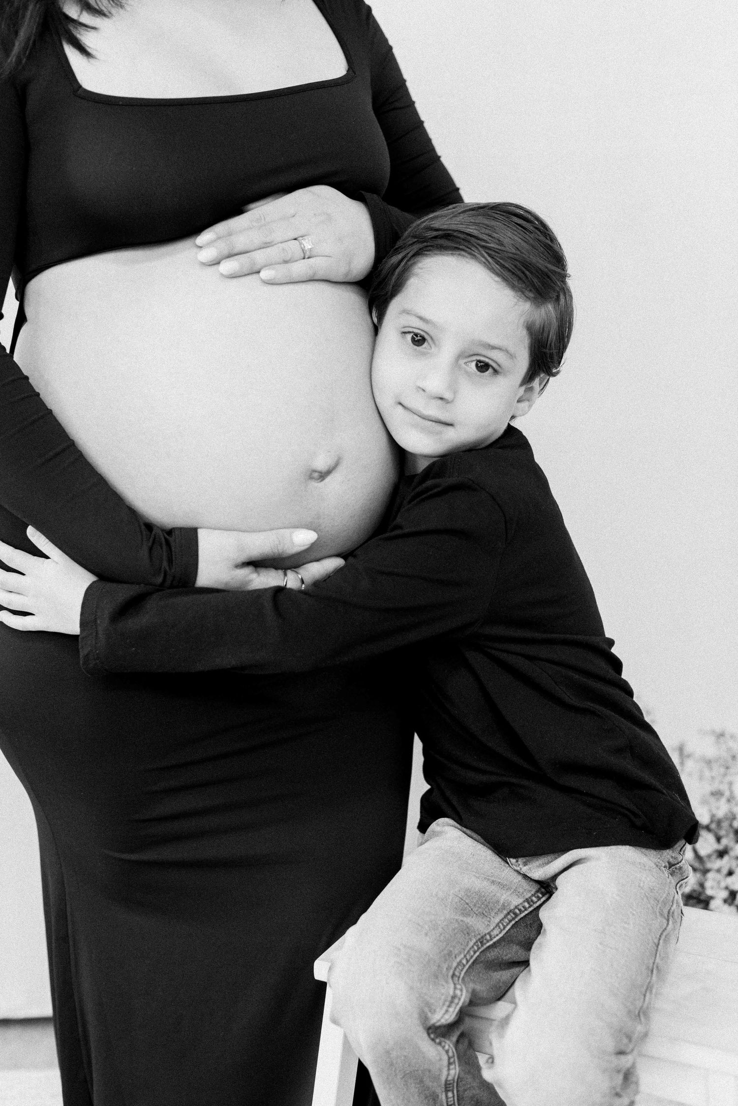 Black and white maternity photo showing child hugging pregnant belly.
