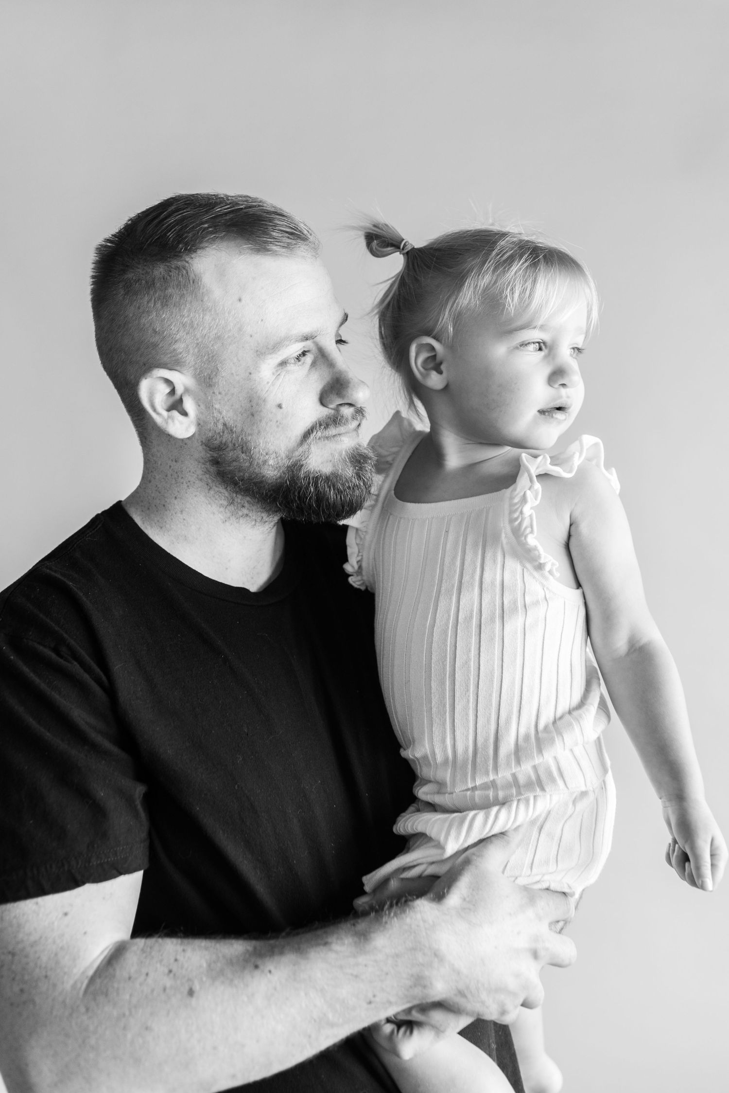 Black and white portrait of family bonding moment against simple backdrop.