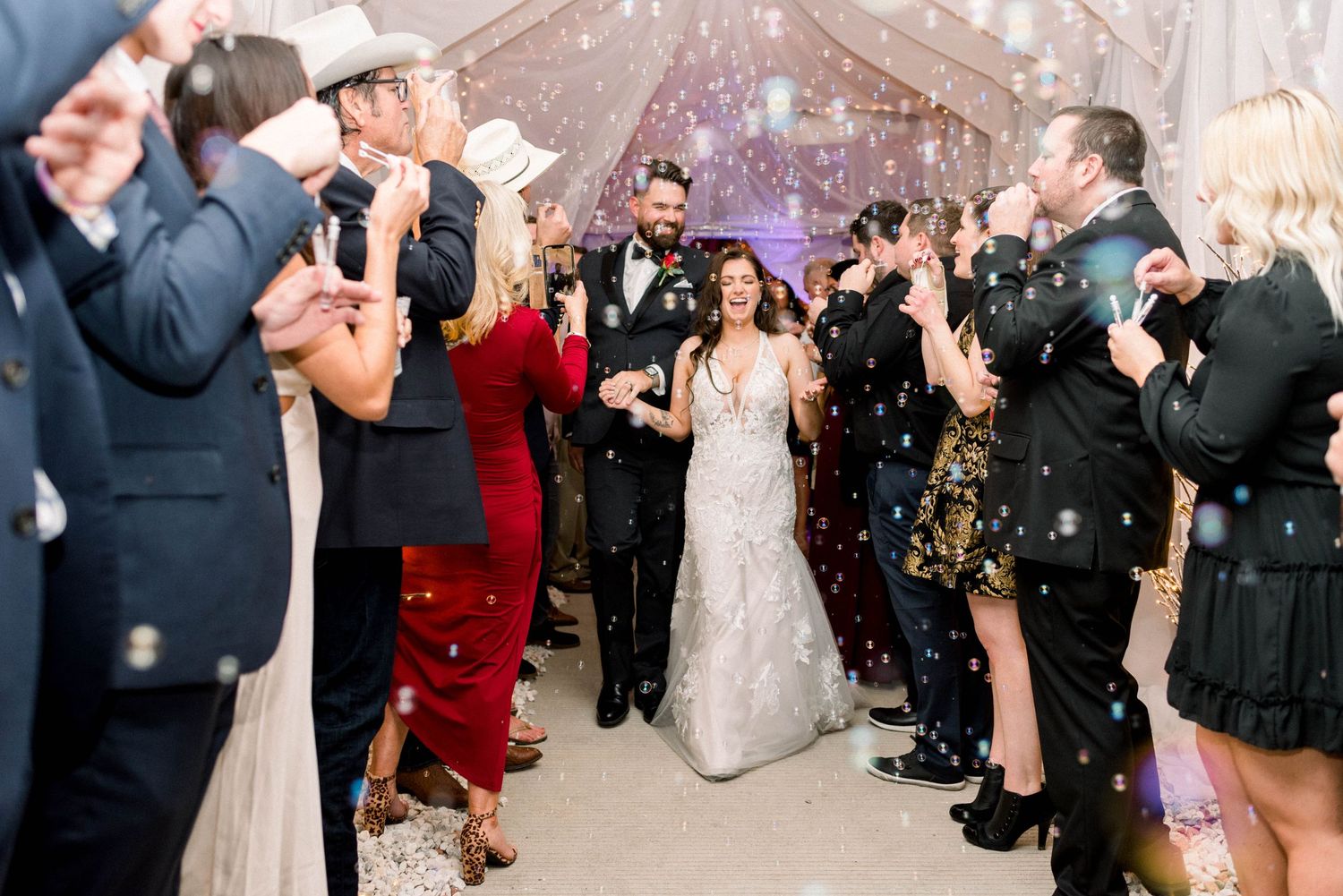 Wedding guests throw confetti over the couple during their celebration exit under a white tent.