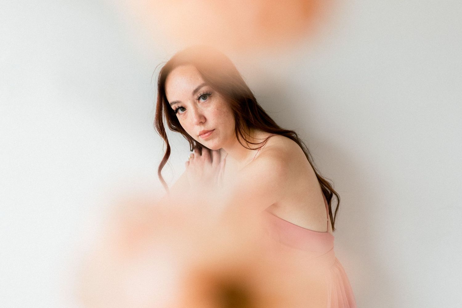 Artistic portrait with soft focus and bokeh effects highlighting gentle pose against white background.