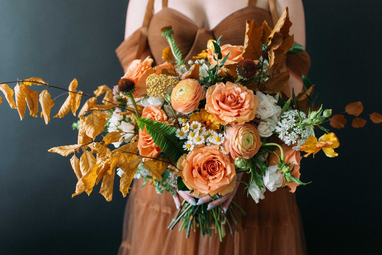 Close-up of luxurious peach rose bouquet with autumn foliage against black backdrop.
