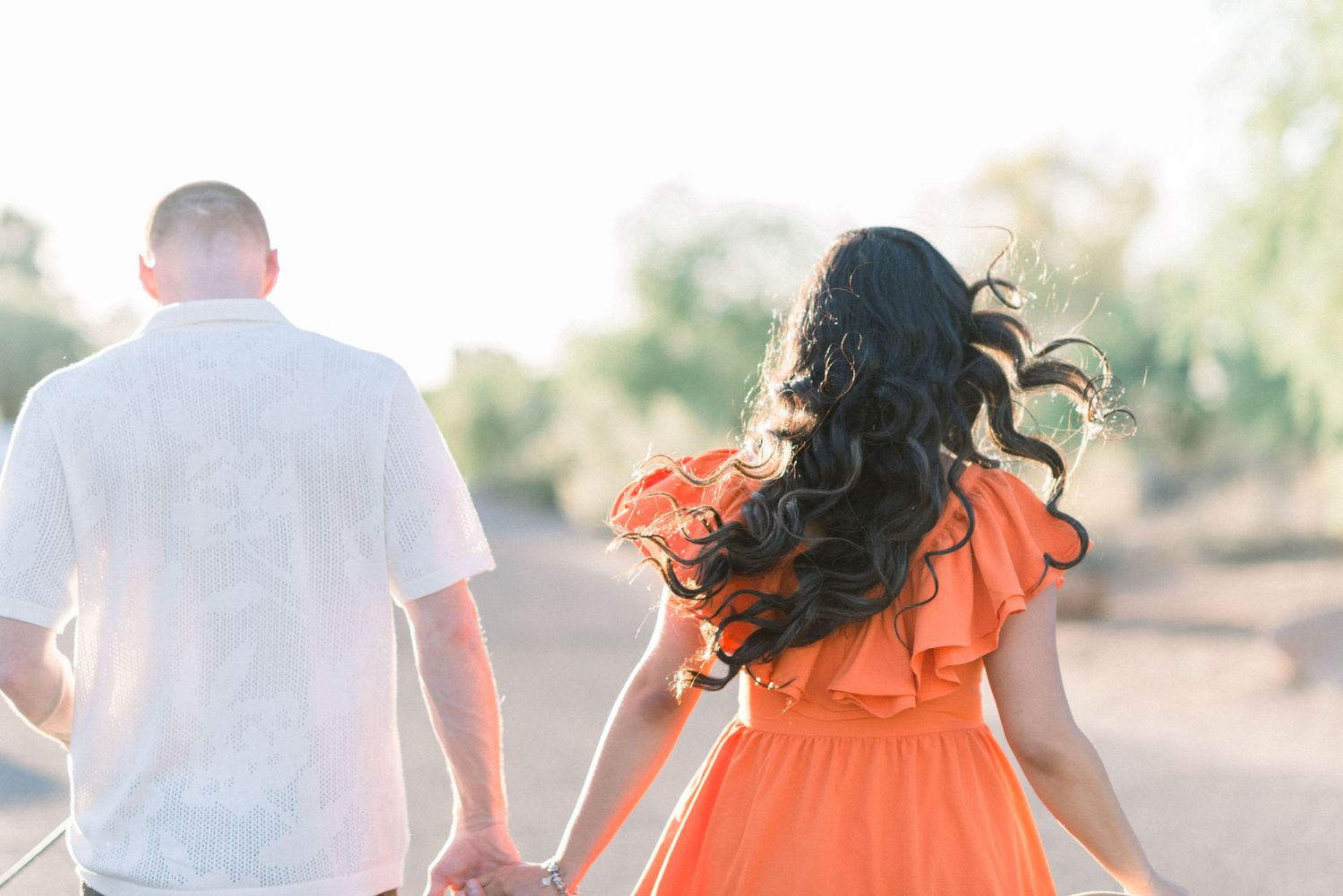 Back view of couple walking together, her dress flowing in orange against his white shirt.