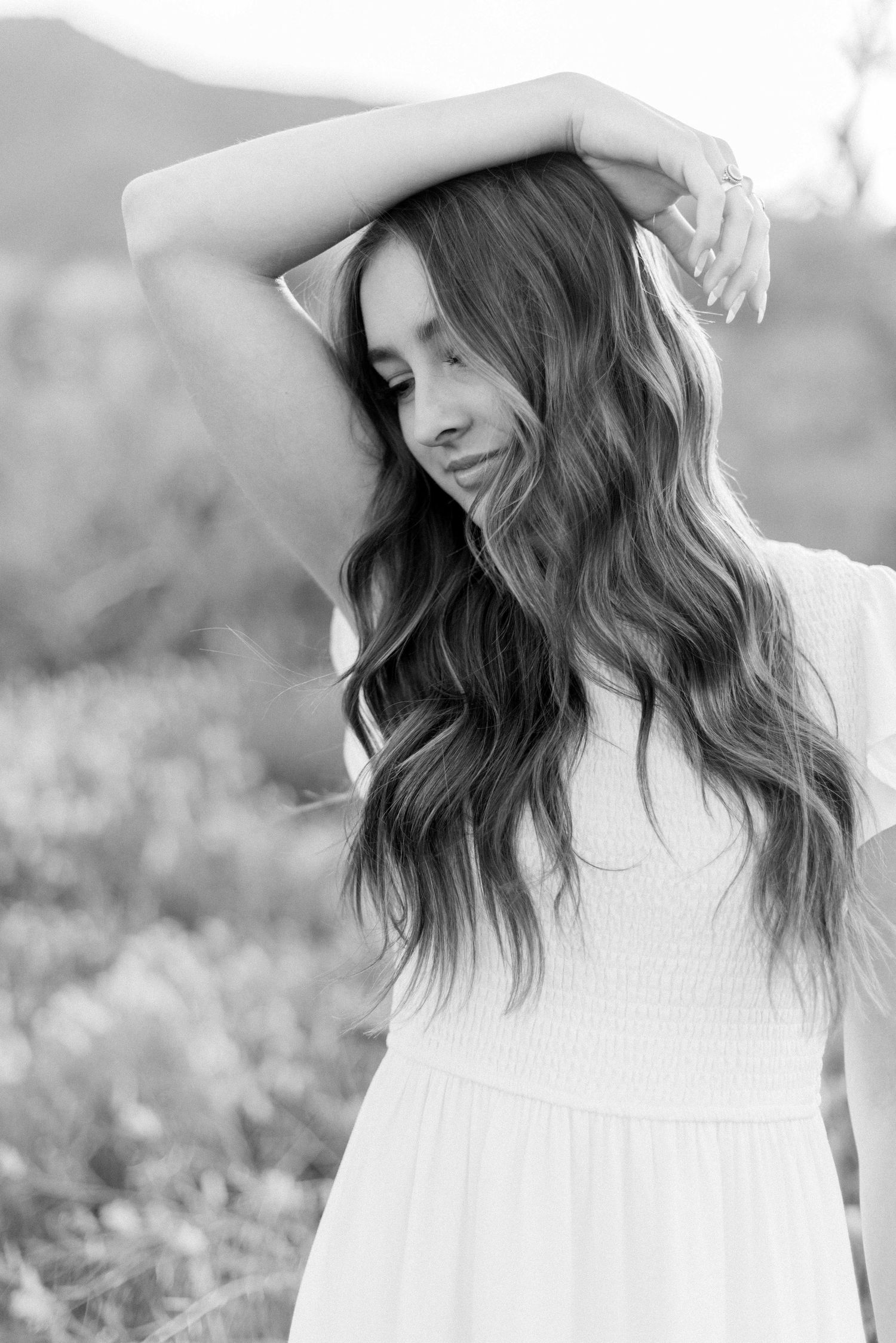 Black and white portrait with flowing hair and white dress against natural backdrop.