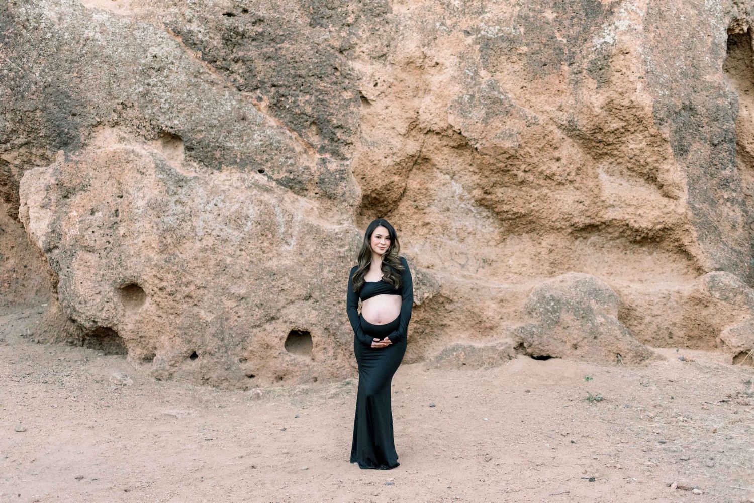Elegant maternity silhouette posed against dramatic rock formations in a desert setting.