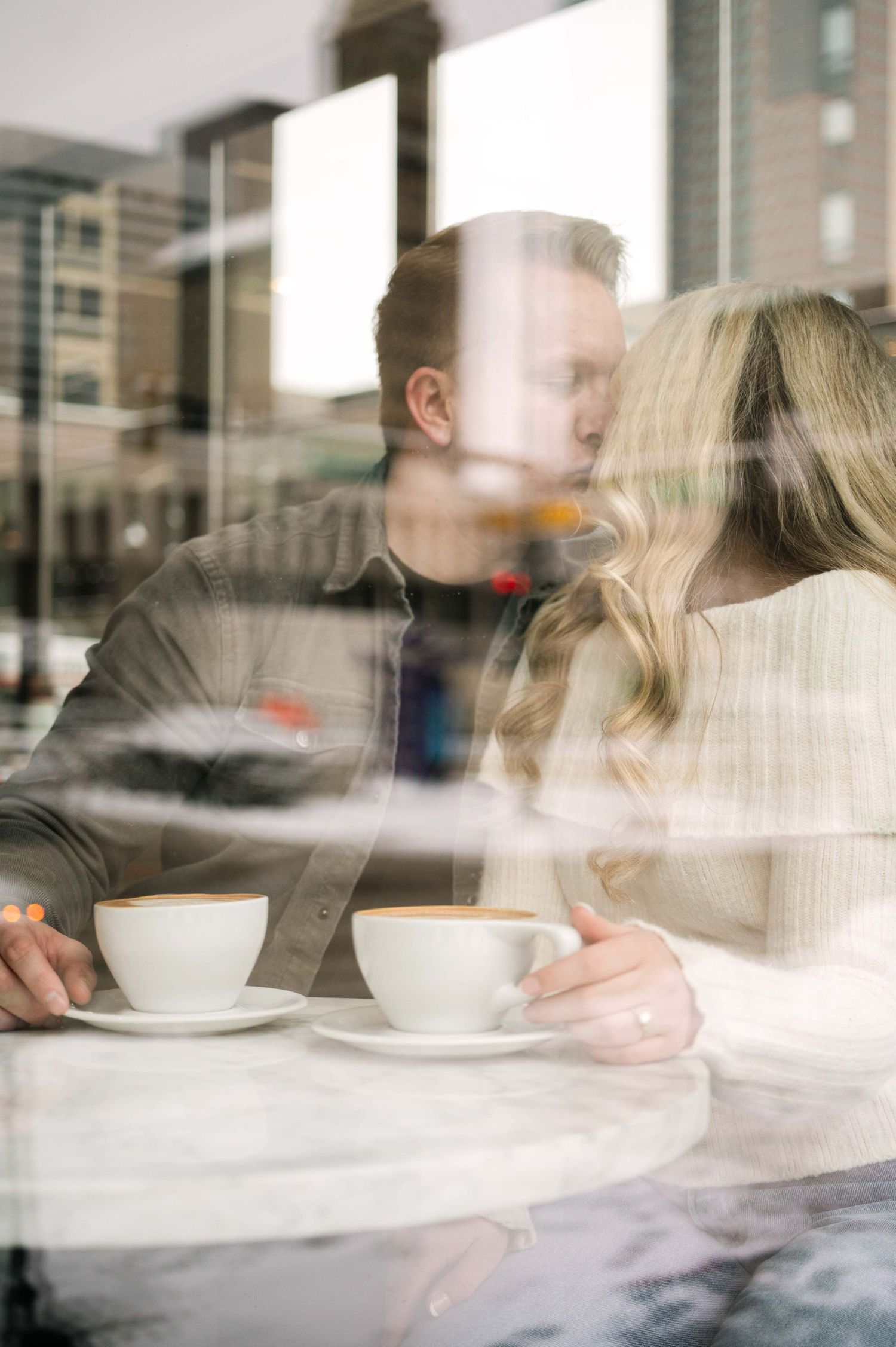 A romantic coffee date captured through cafe window reflections.