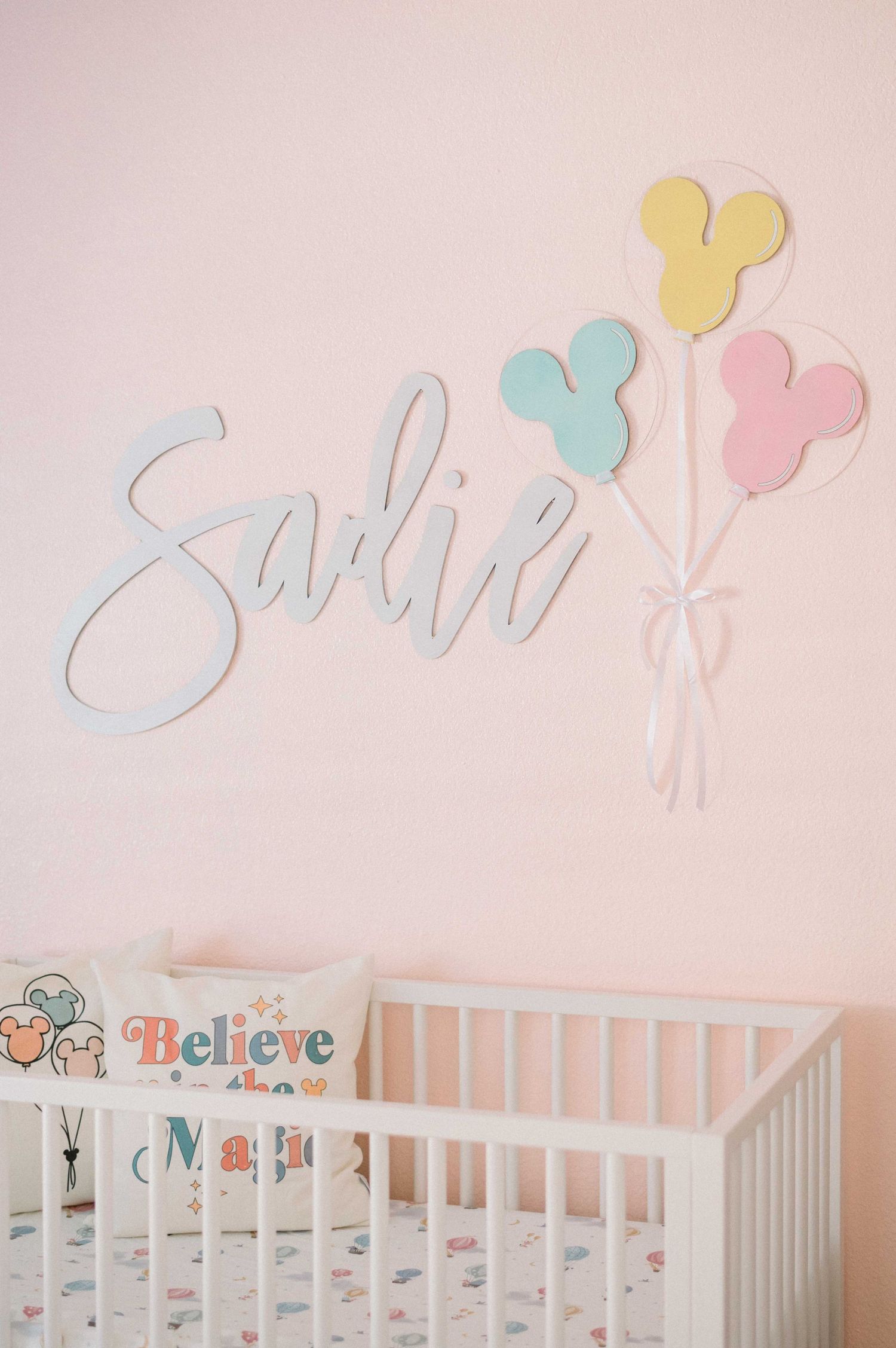 Pink nursery wall decorated with name 'Sadie' and pastel Mickey Mouse balloon cutouts.