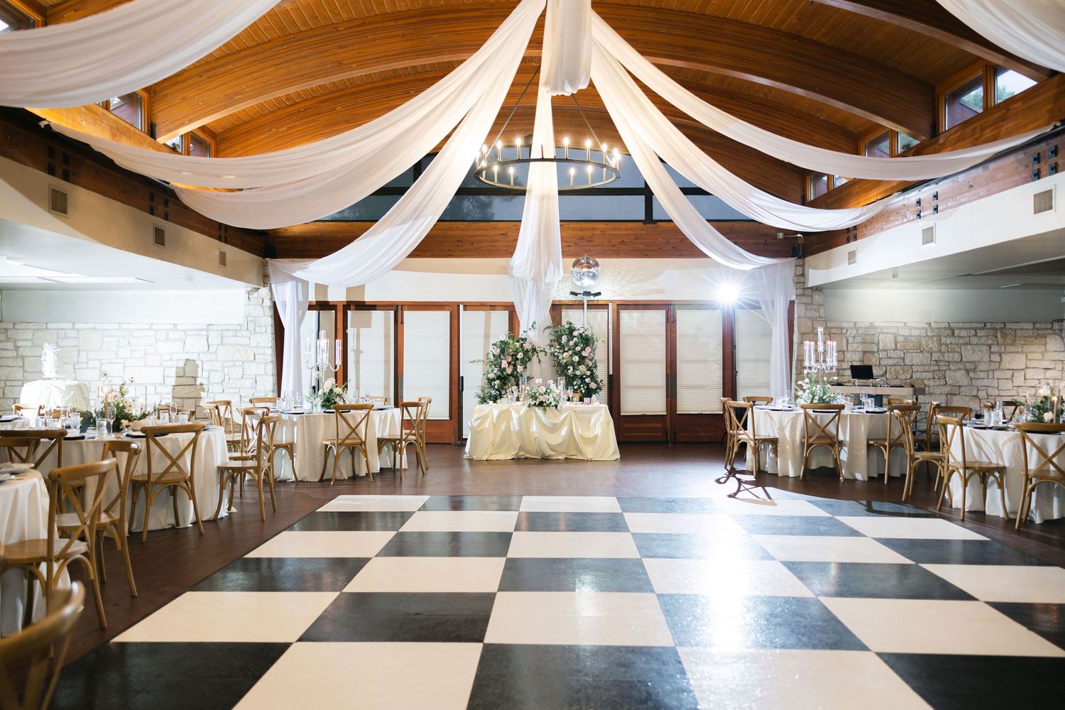 An elegant reception venue with draped white fabric and checkerboard dance floor.