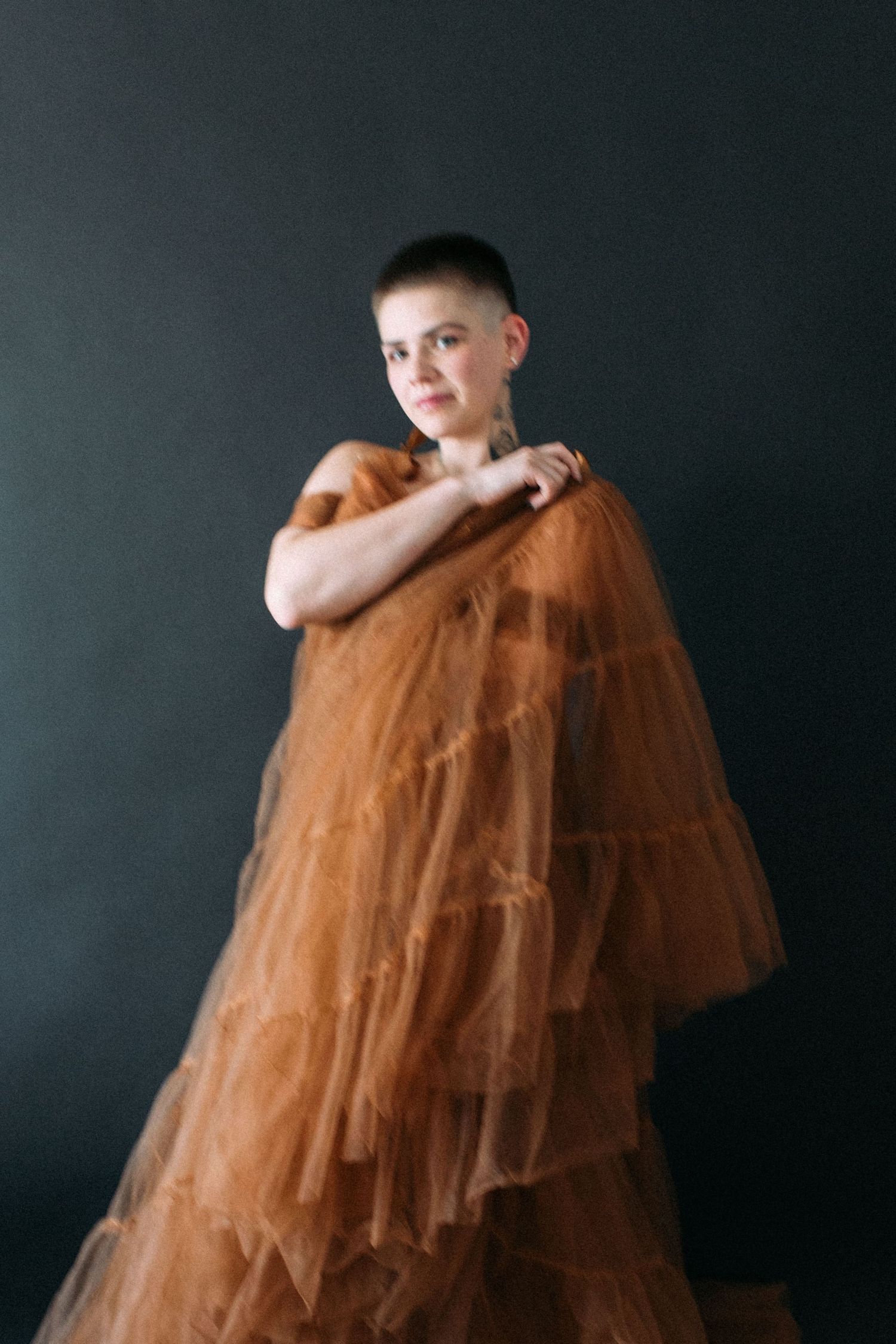 Artistic portrait in brown tulle dress against dark studio backdrop.