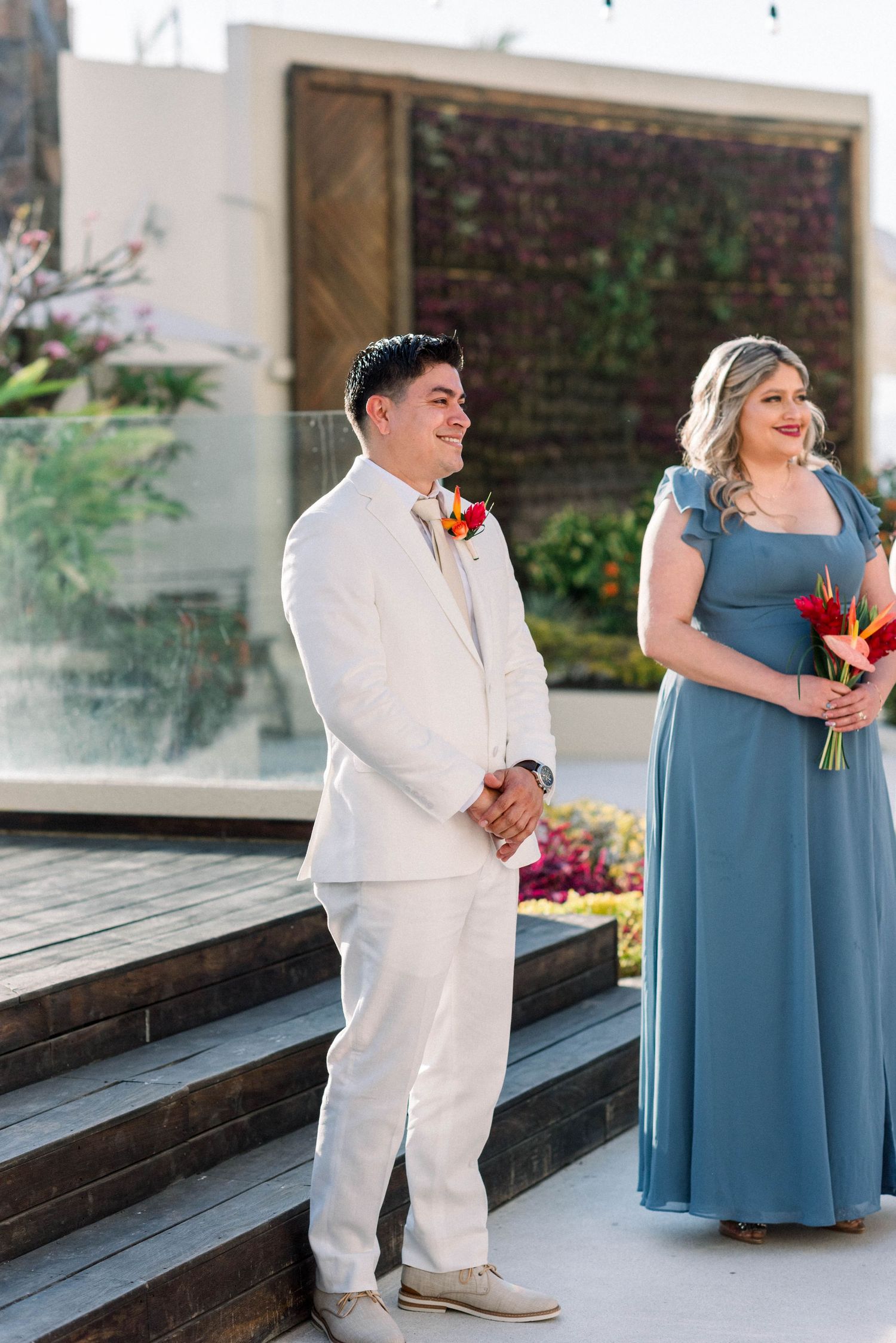 Wedding party members in white suit and blue dress standing at decorated outdoor venue.