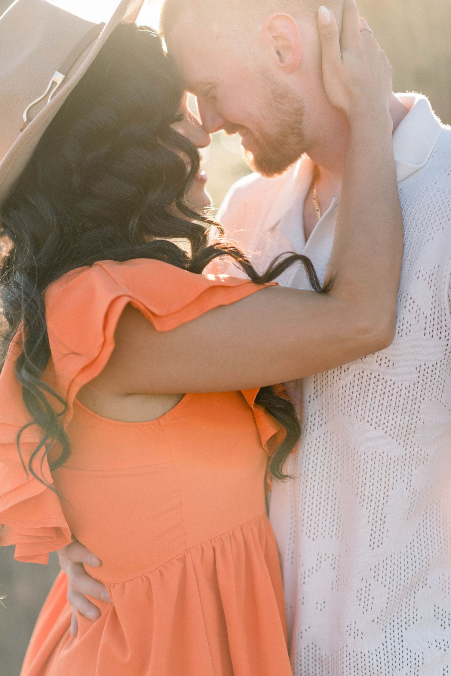 Intimate moment between couple in orange dress and white shirt during golden hour photoshoot.