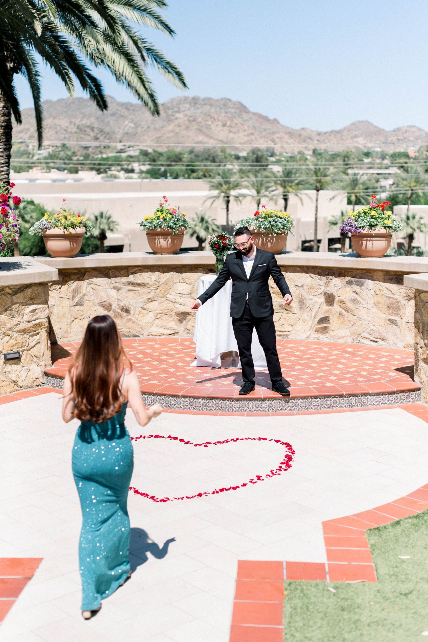 Romantic proposal setup with heart made of rose petals on terrace overlooking desert mountains.