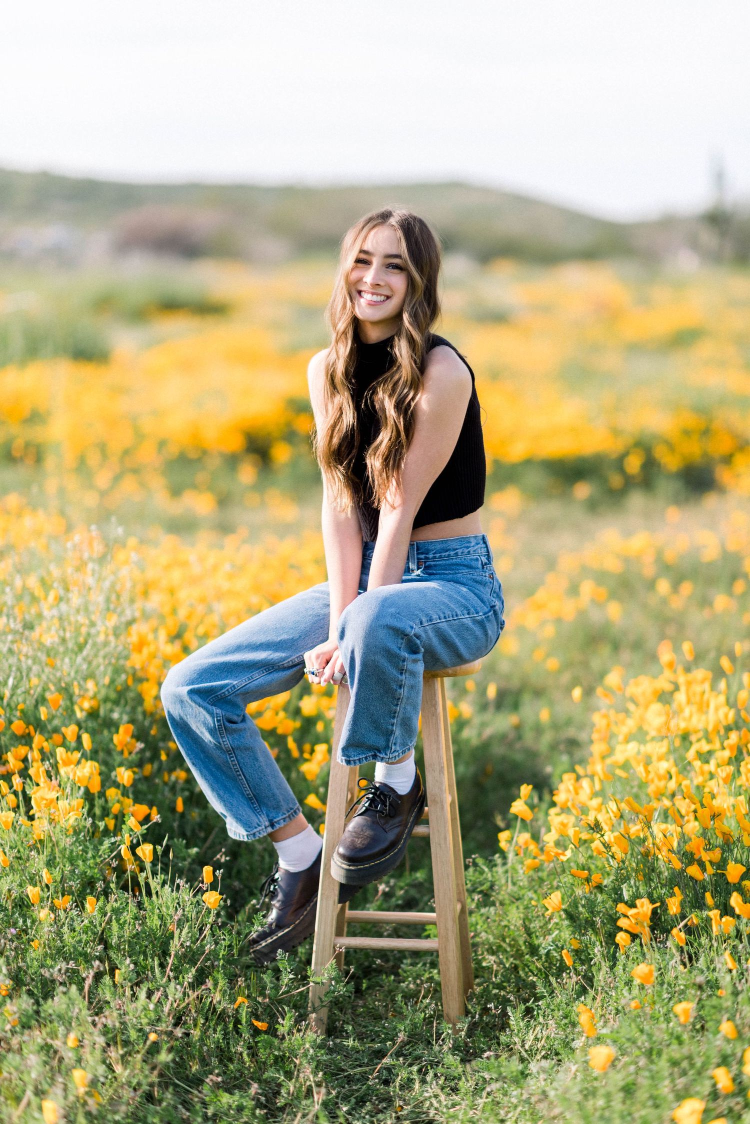 Casual portrait in a field of yellow wildflowers while sitting on a wooden stool.