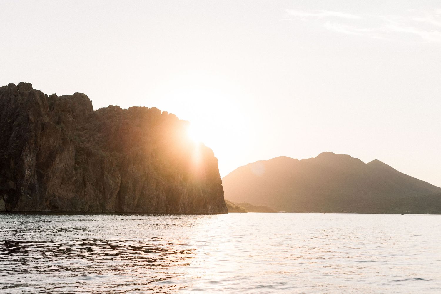Dramatic sunset over rocky coastal cliffs creates silhouettes against golden sky and ocean waves.