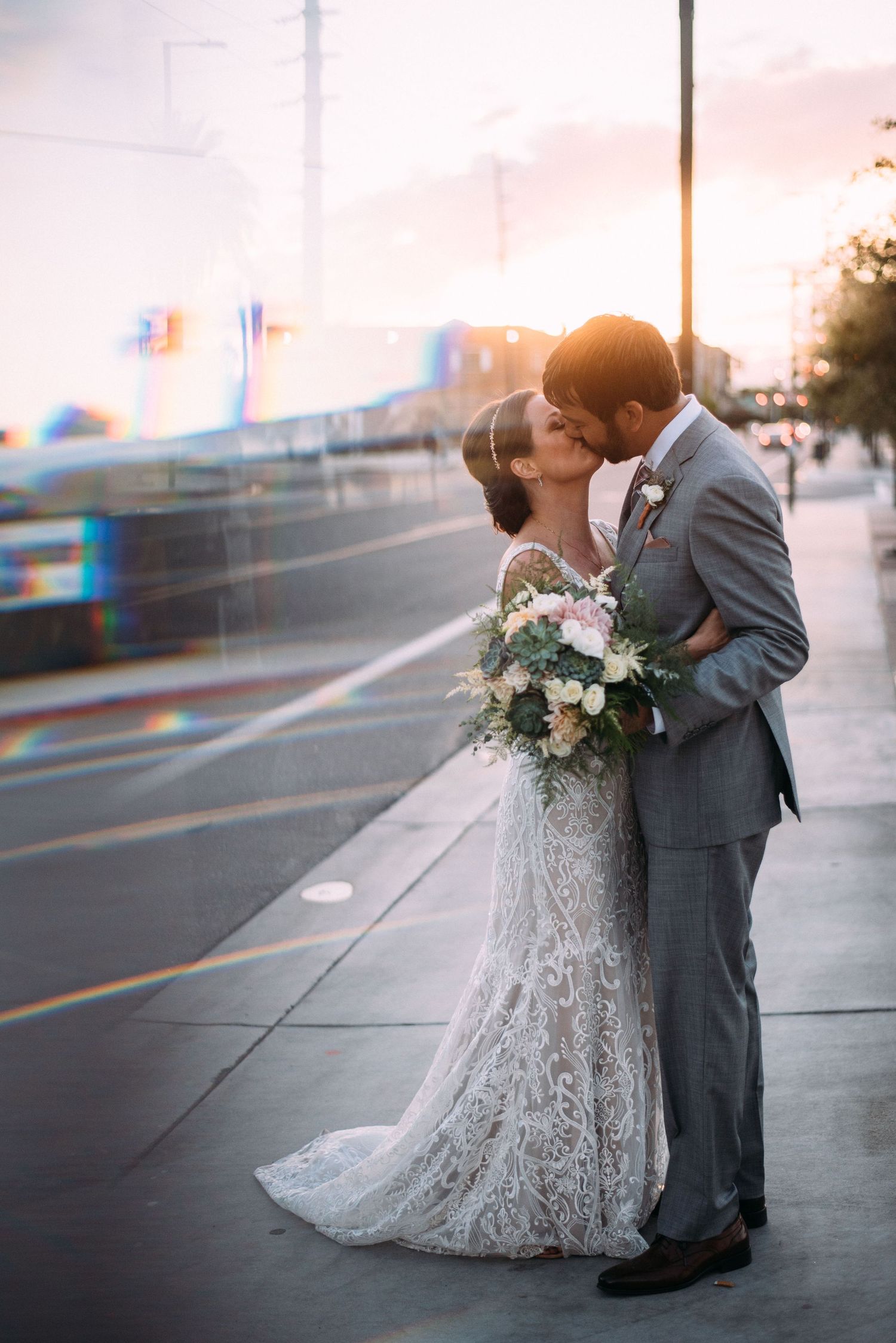 Romantic sunset wedding portrait on urban street with city lights in background.