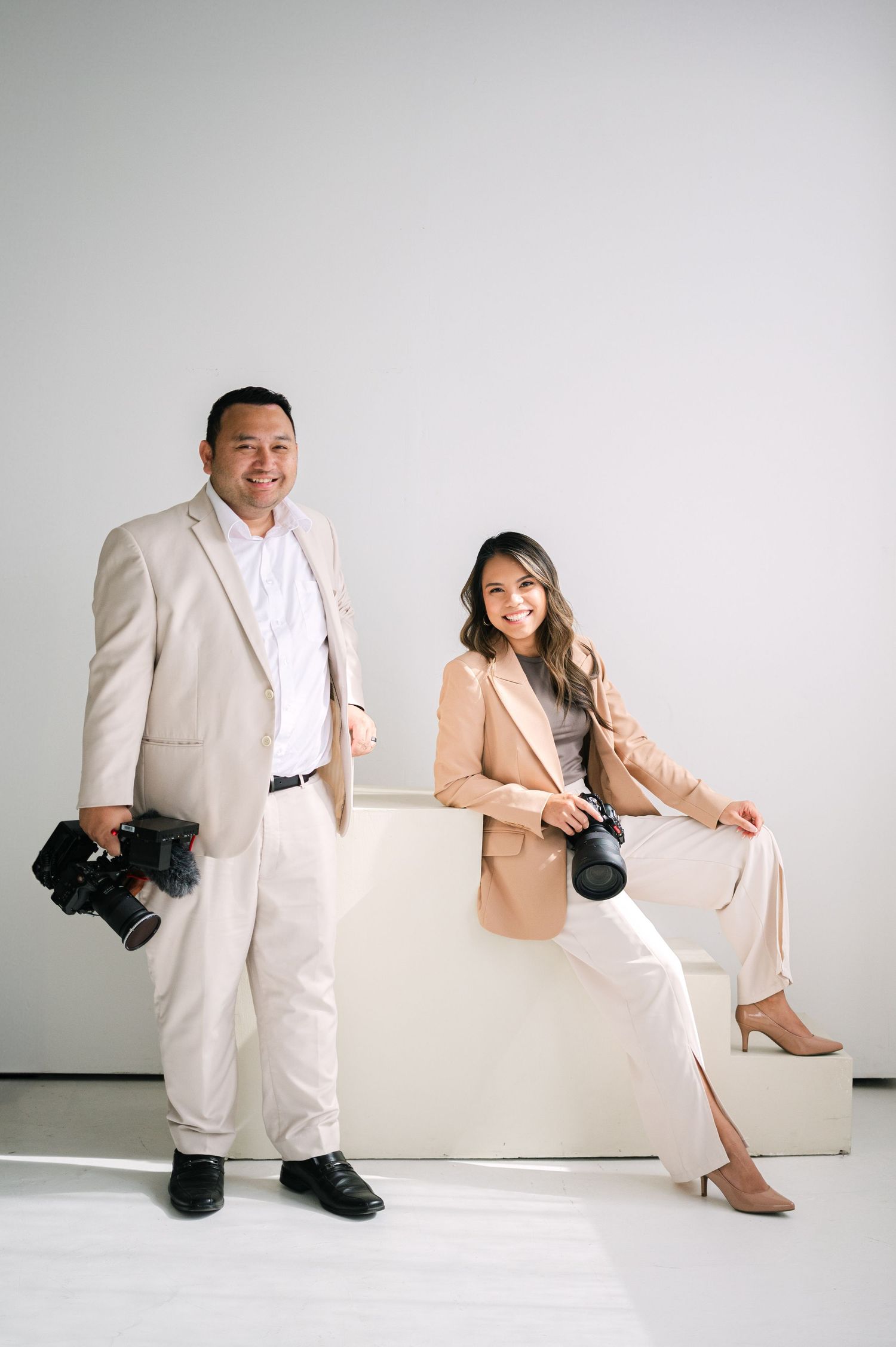 Professional photography session with two people in cream colored suits against a white studio backdrop.